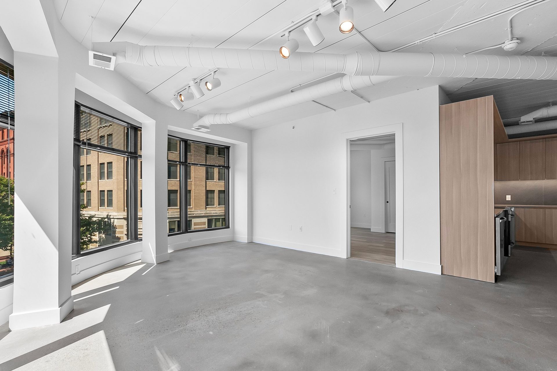 Empty, bright room with large windows, concrete floor, white walls, and exposed ductwork.