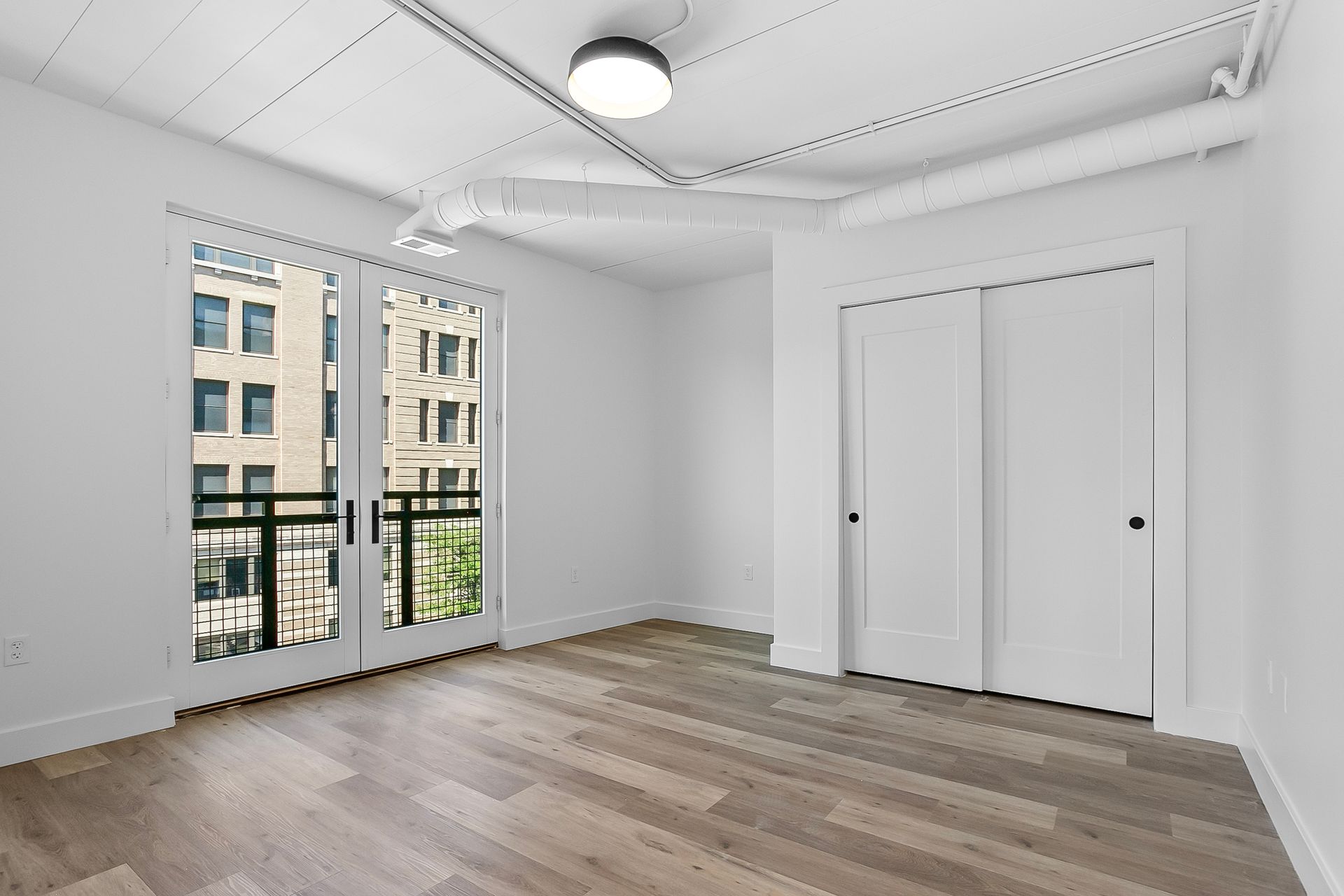 Empty room with balcony doors, white walls, wood floor, and closet.