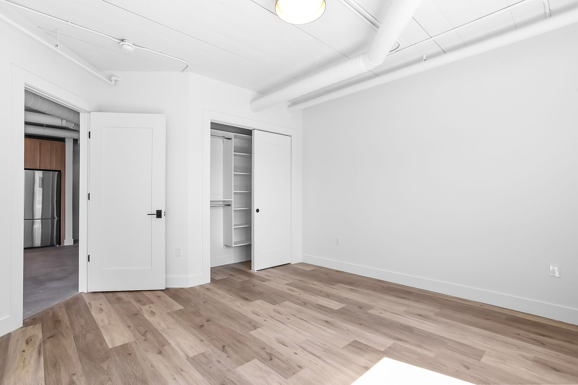 Empty, bright room with hardwood floors, white walls, and two doors; one to closet.