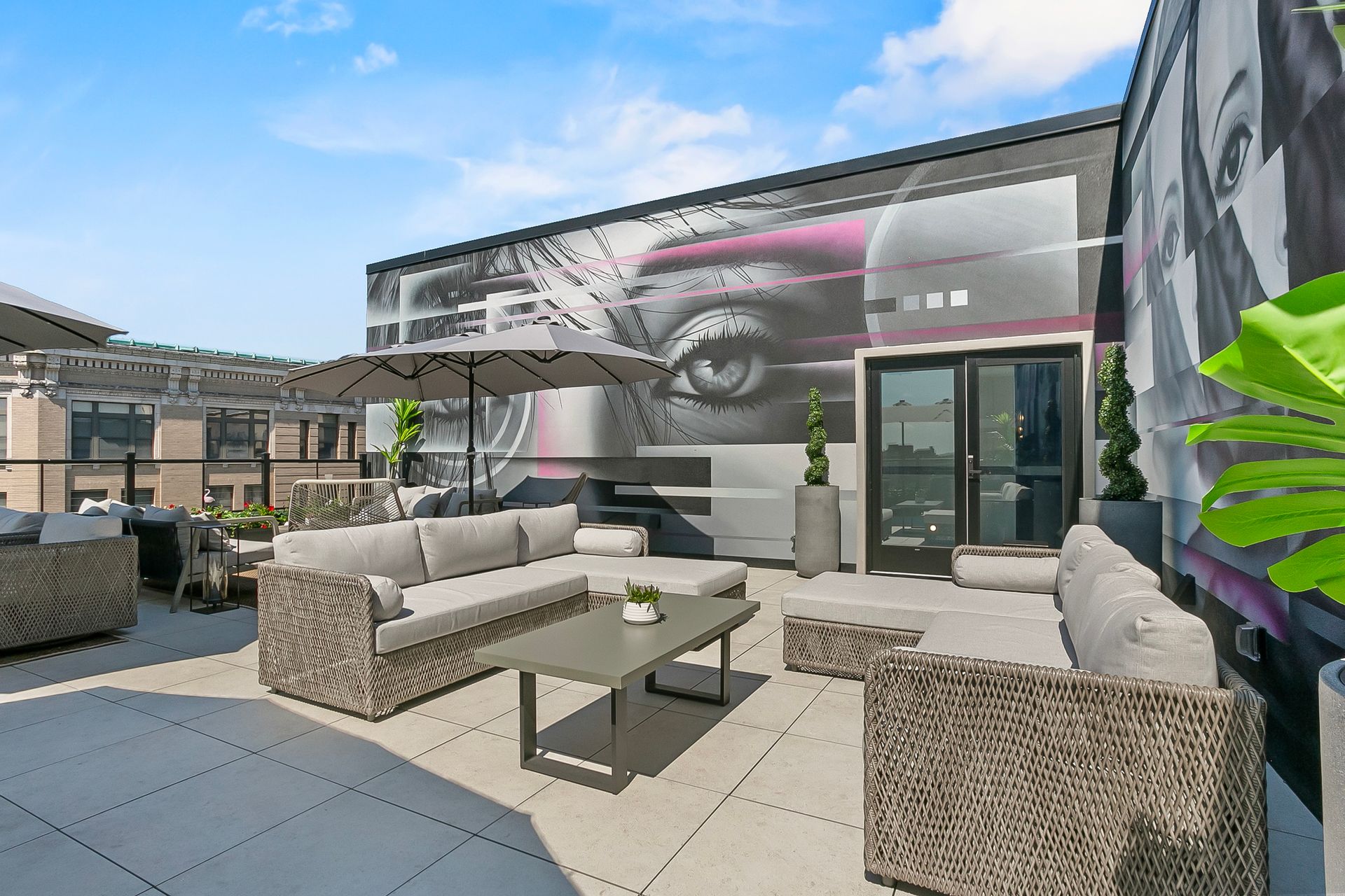 Rooftop patio with wicker furniture, a mural, and an umbrella, under a blue sky.