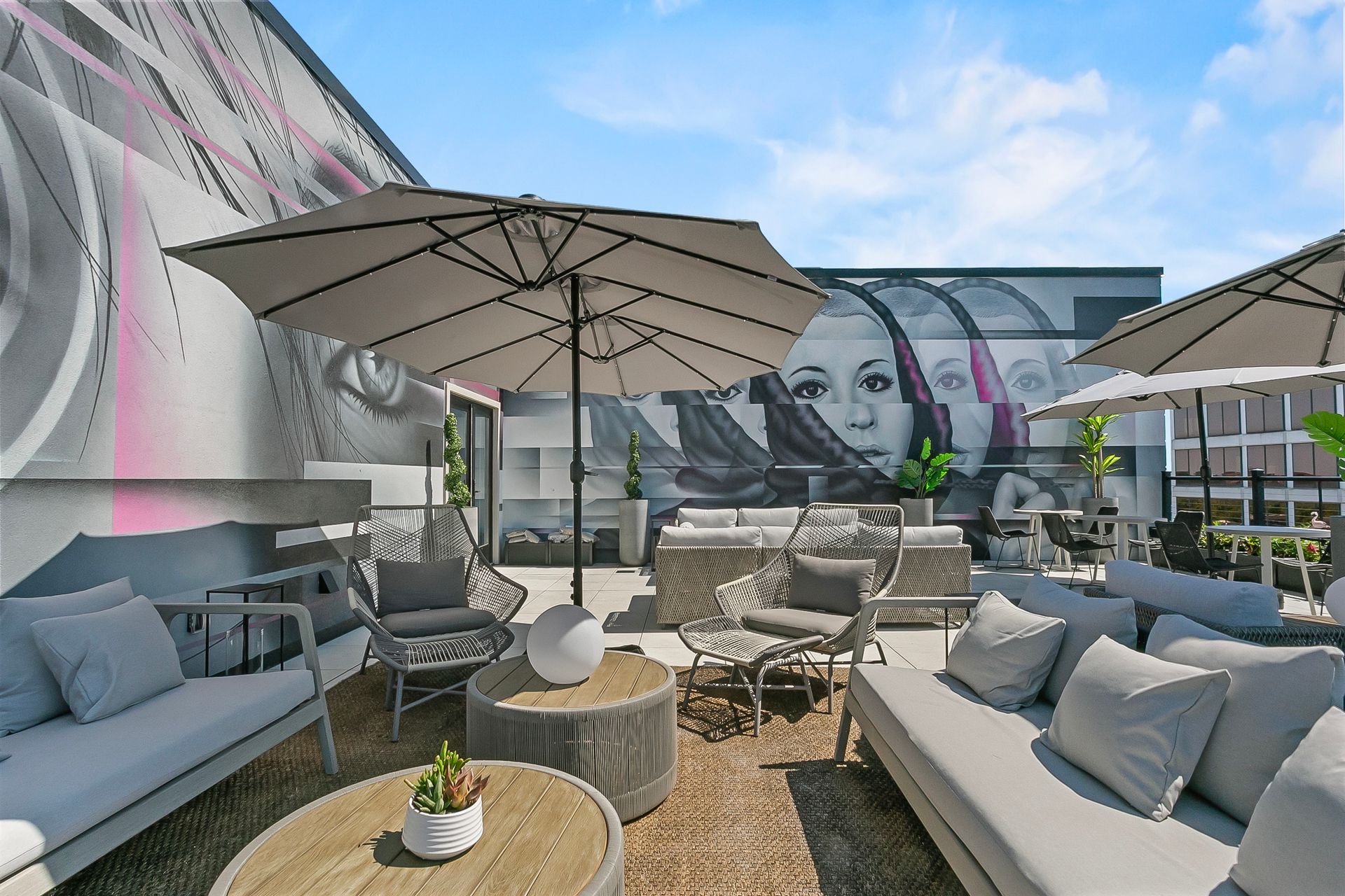 Outdoor lounge area with gray furniture, umbrellas, and a mural on the wall.