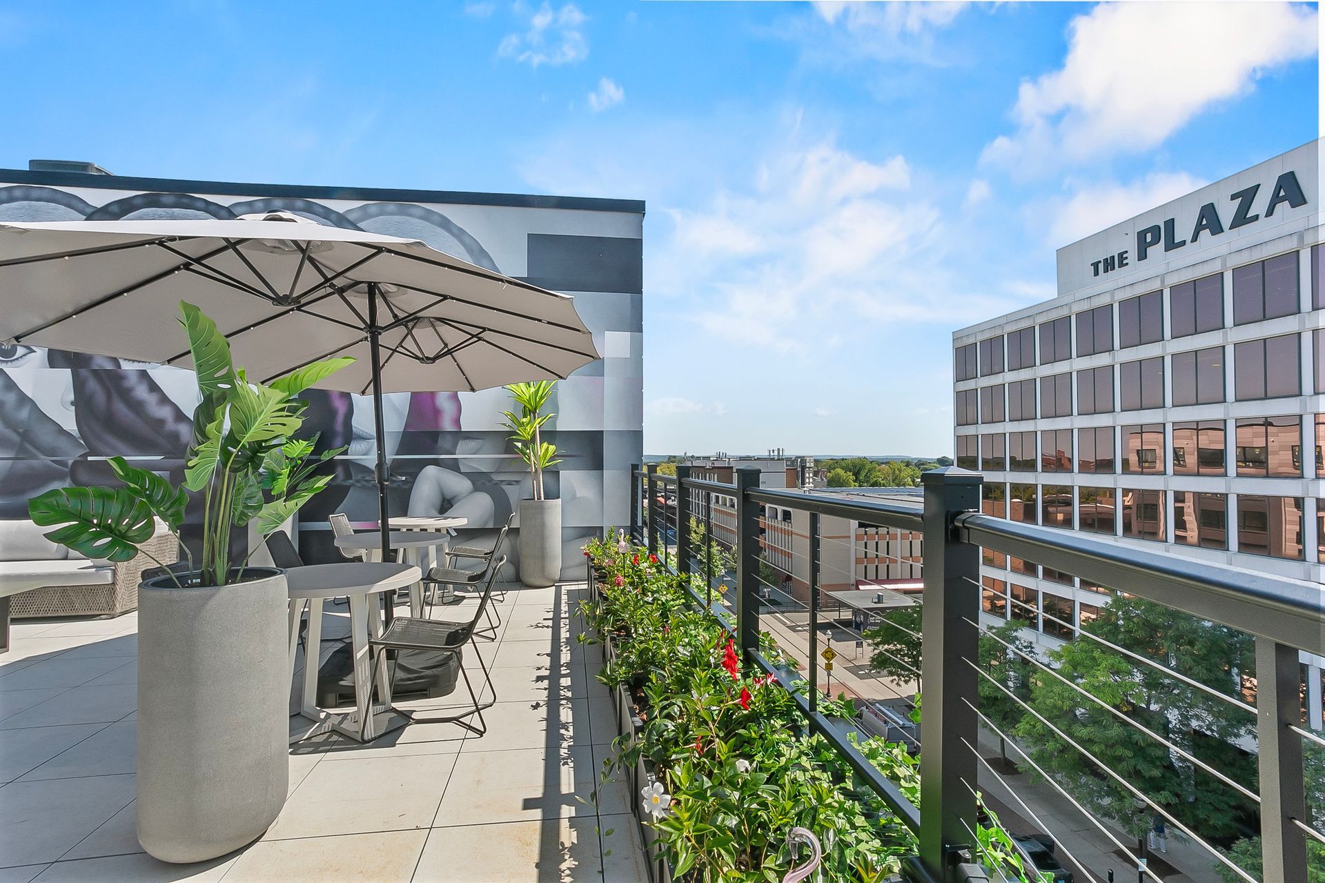 Rooftop patio with umbrella, tables, plants, and a view of the city and