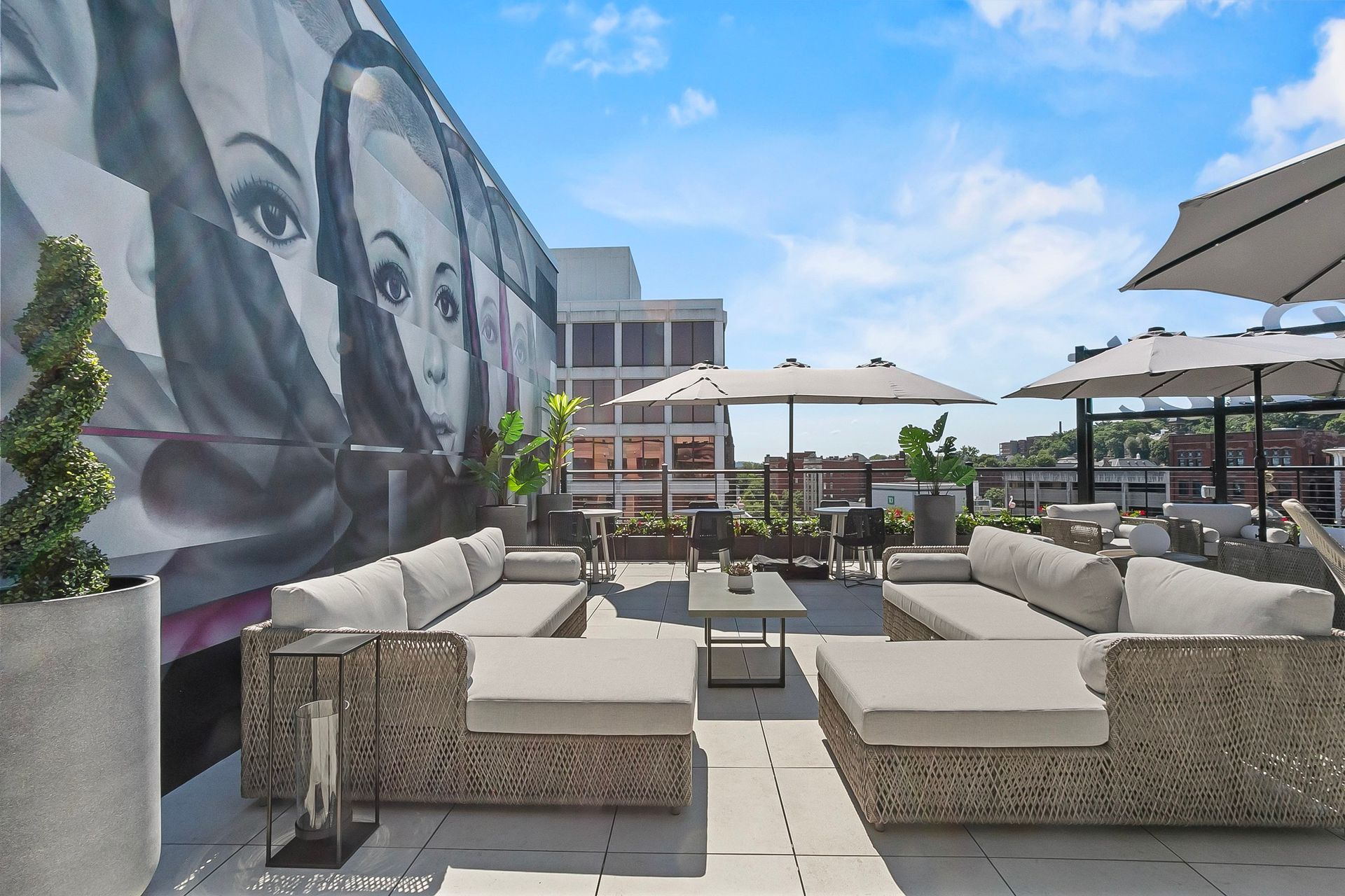 Rooftop patio with gray sofas, tables, umbrellas, and a mural of a woman against a blue sky.