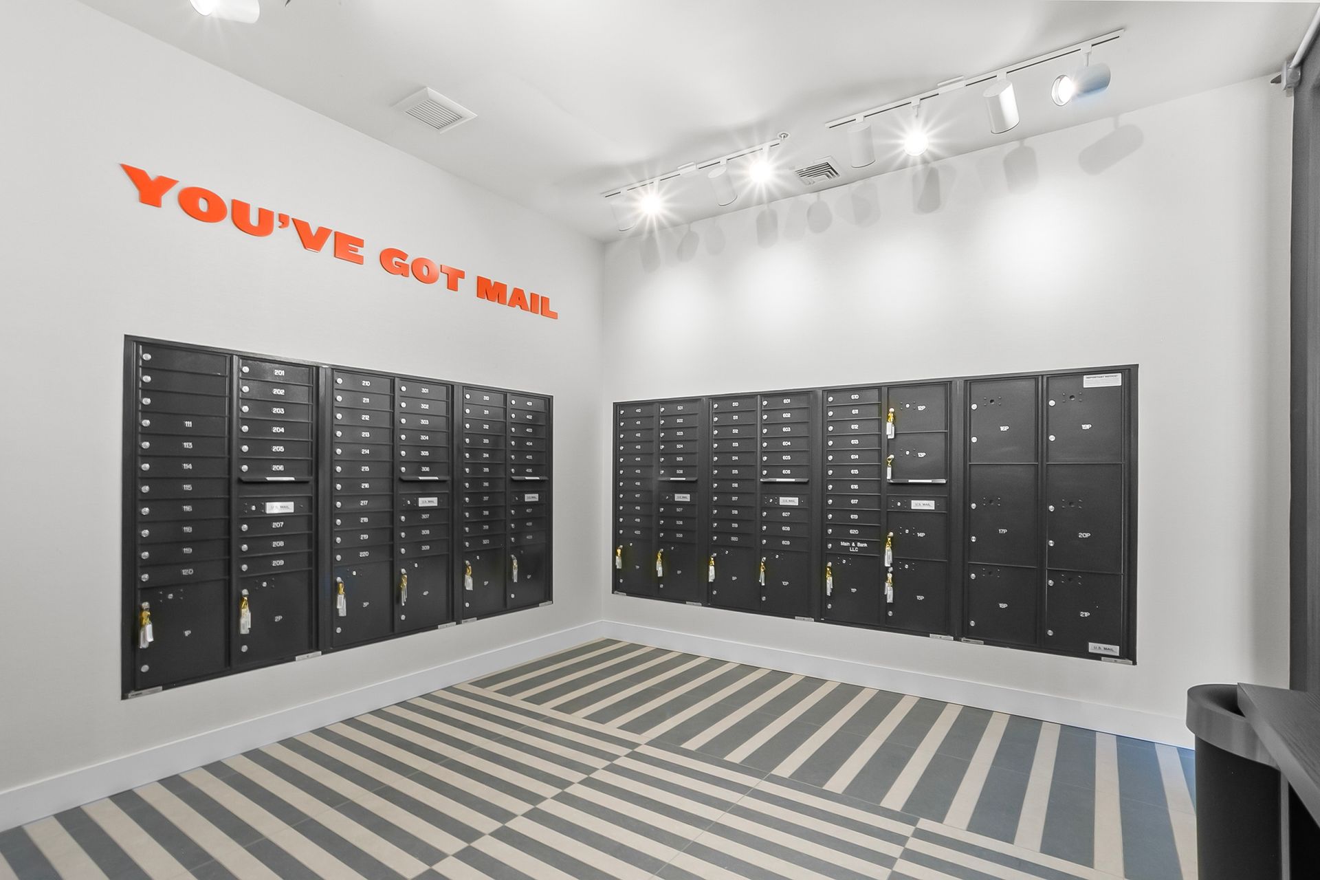 Mailboxes in an apartment lobby with gray and white striped floor and orange text that reads