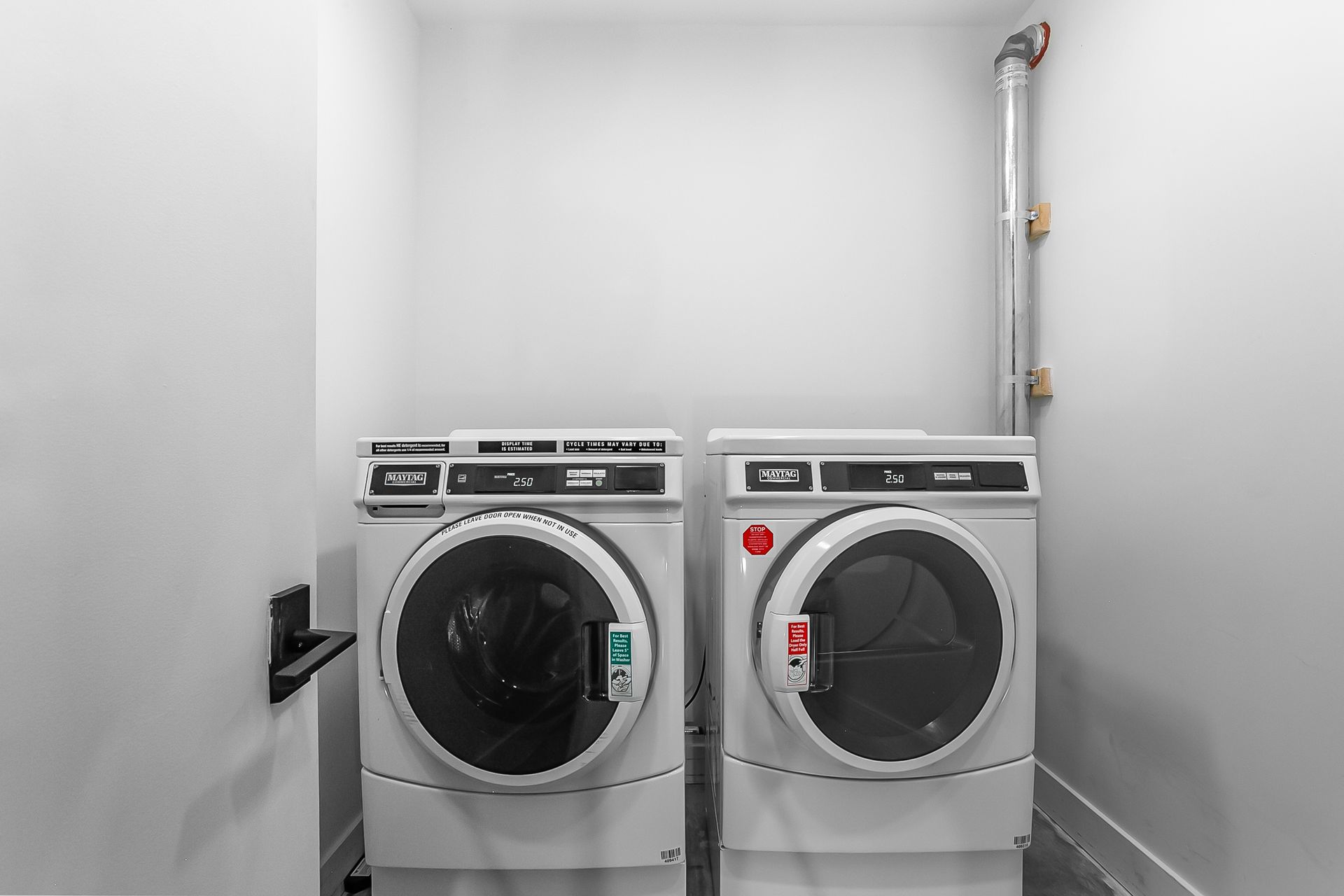 Two commercial washing machines and a dryer in a small, white utility room.