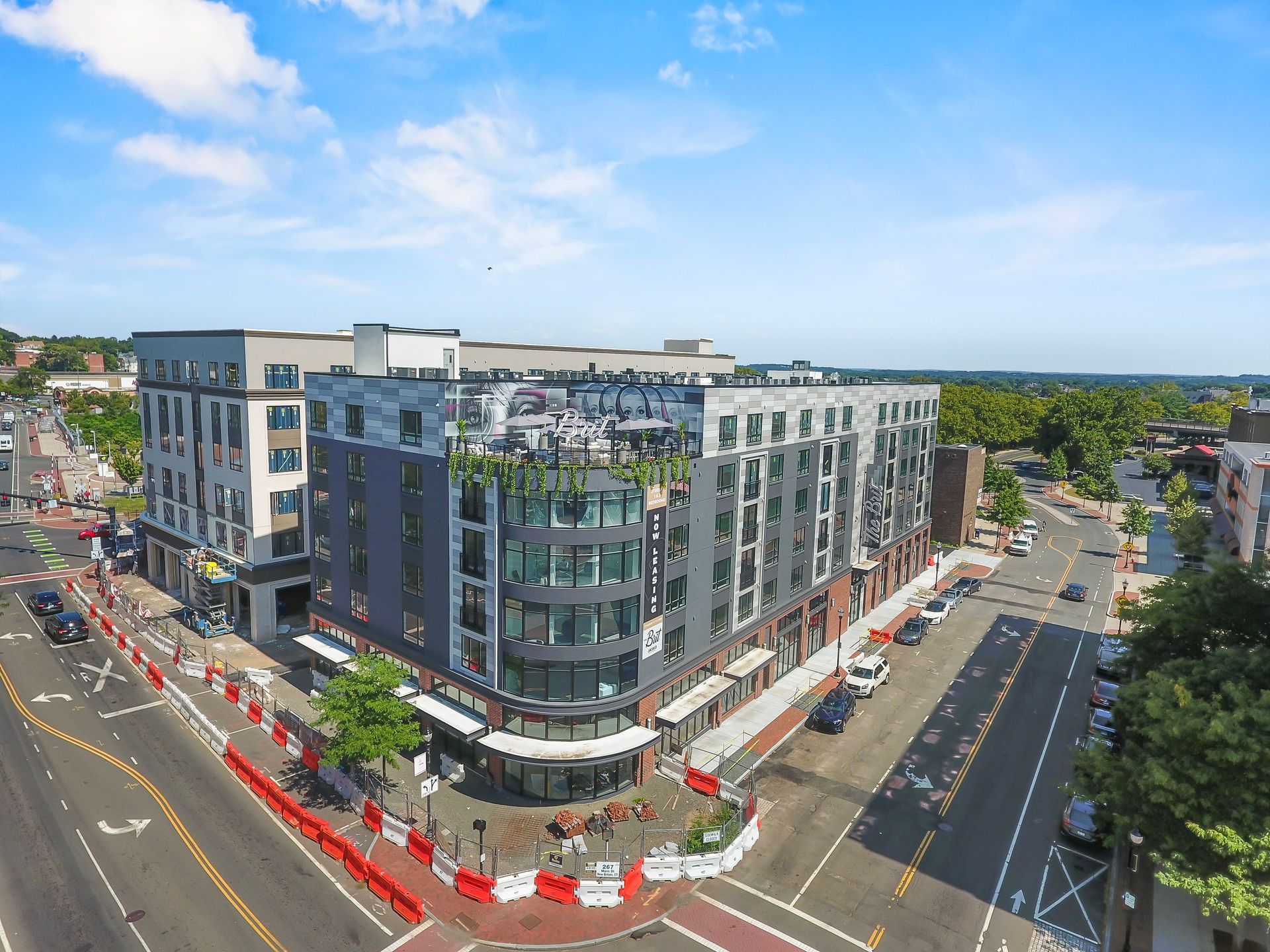 Aerial view of a multi-story modern building at an intersection. Red barriers line the sidewalks.