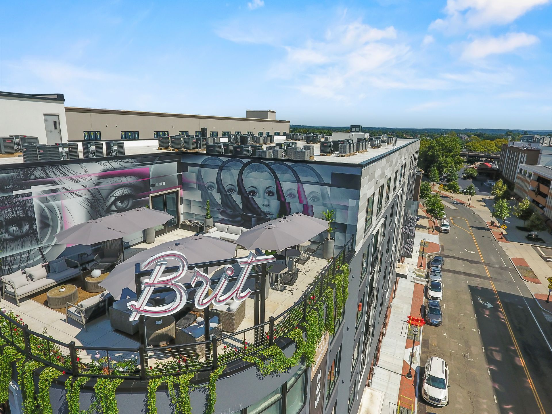 Rooftop bar with mural and seating. Grey umbrellas and cityscape.