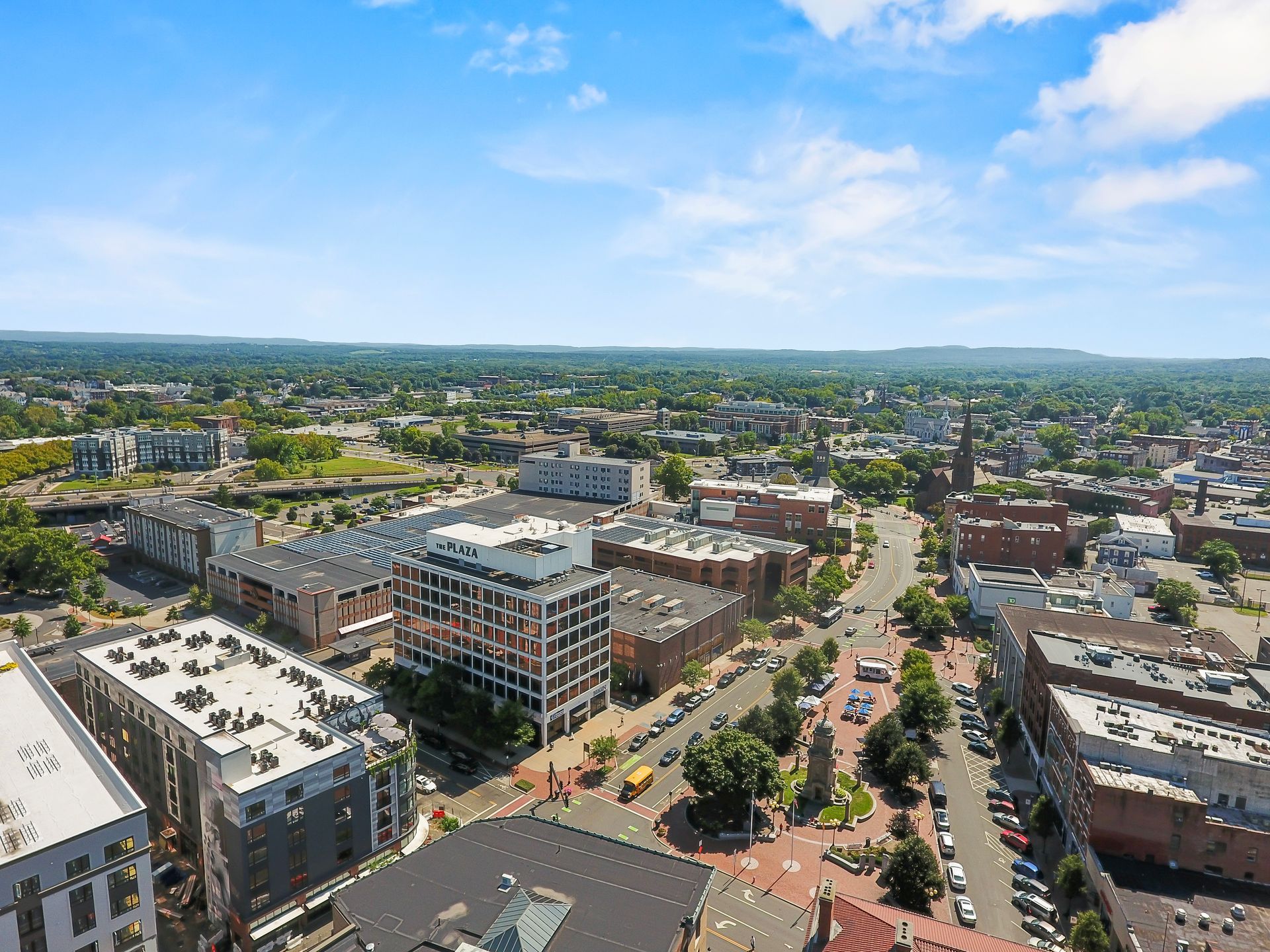 Aerial view of a city with buildings, roads, and a blue sky with clouds.