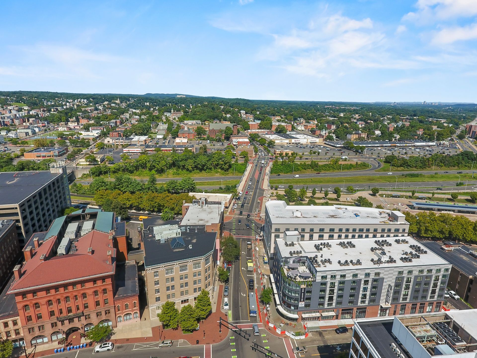 Aerial view of a city street with buildings and a bridge, under a bright blue sky.