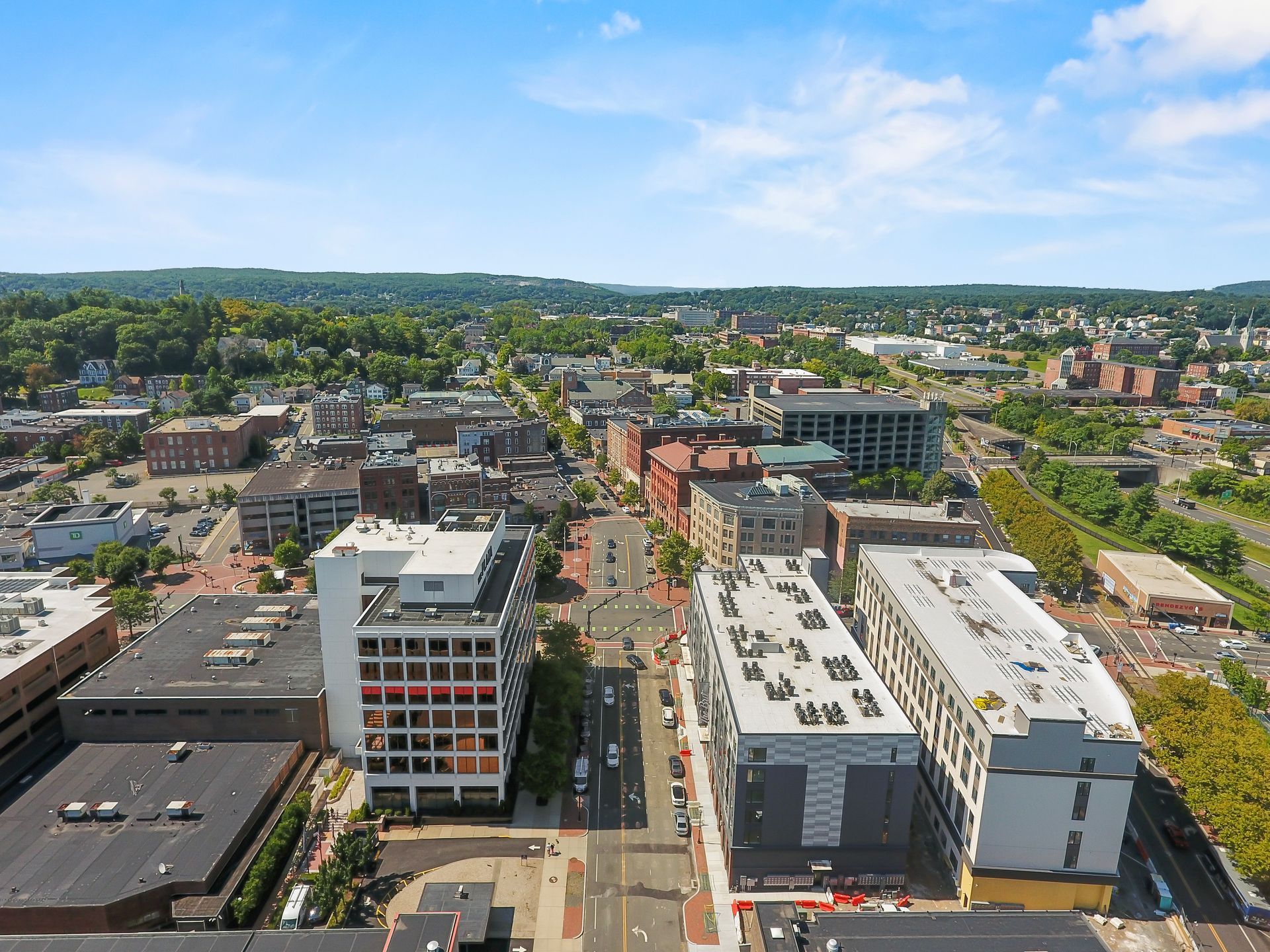 Aerial view of a city street with buildings, trees, and blue sky.