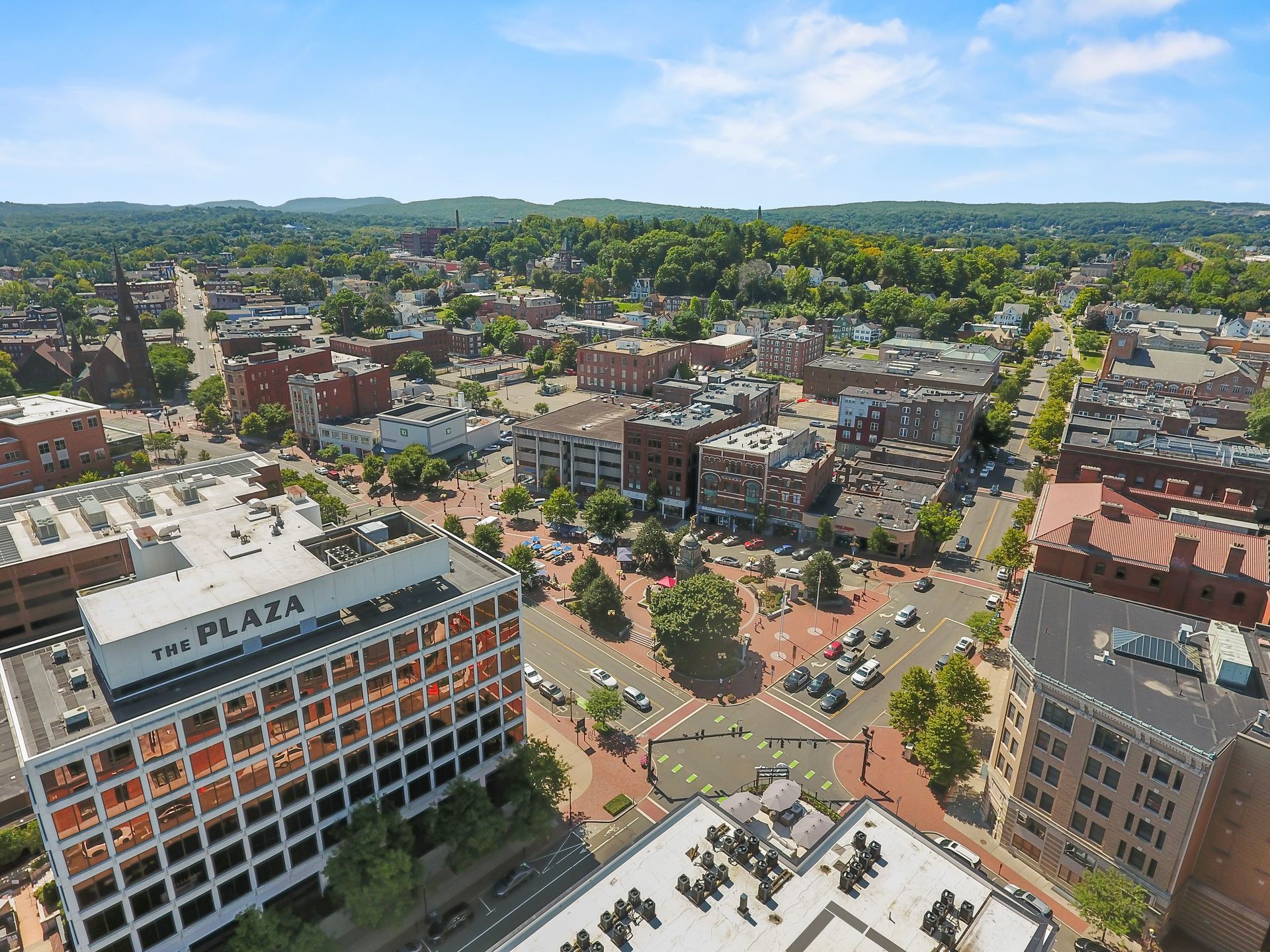Aerial view of a town square with buildings, trees, and roads.