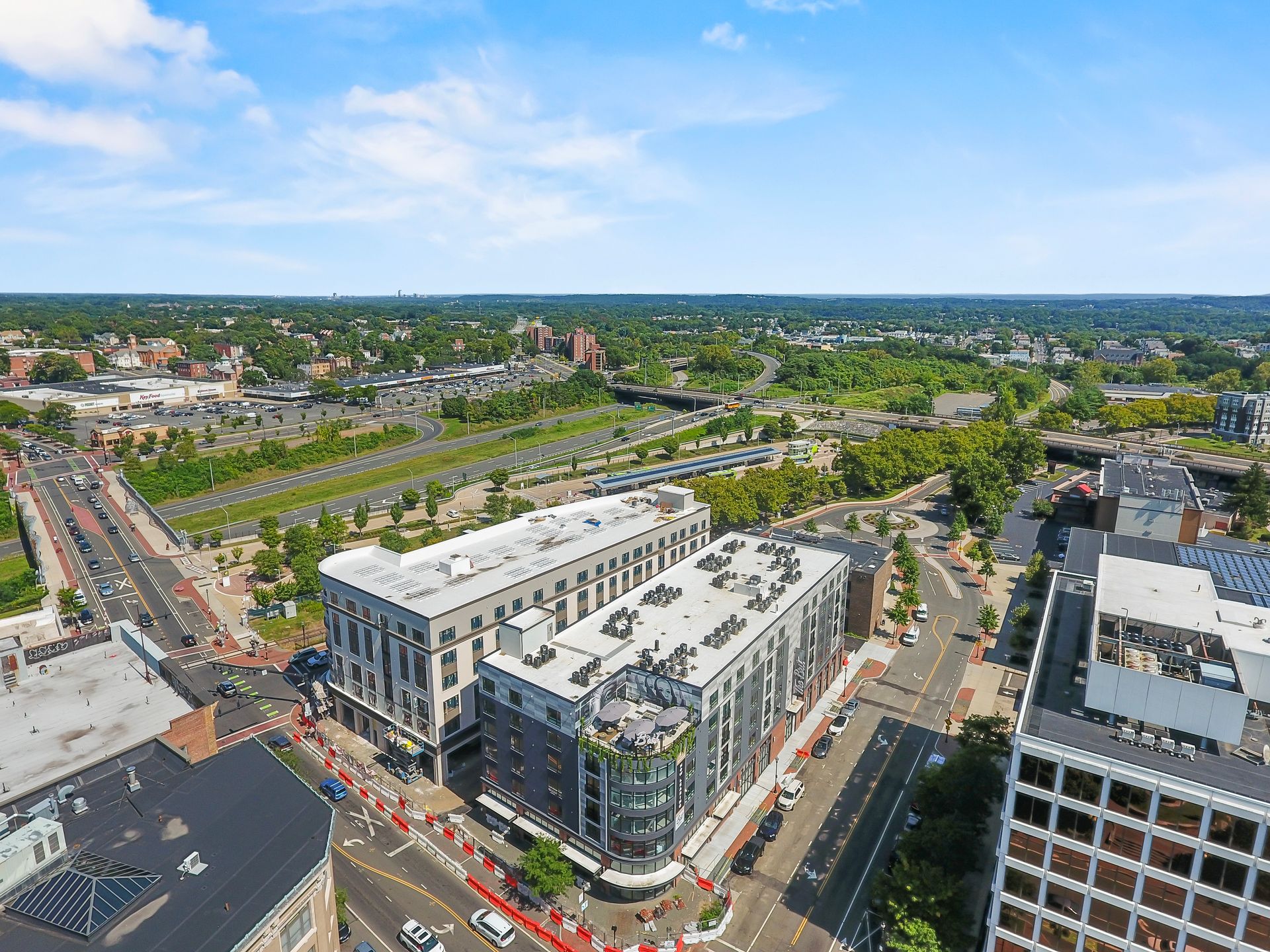 Aerial view of a city with buildings, roads, and green spaces under a blue sky.