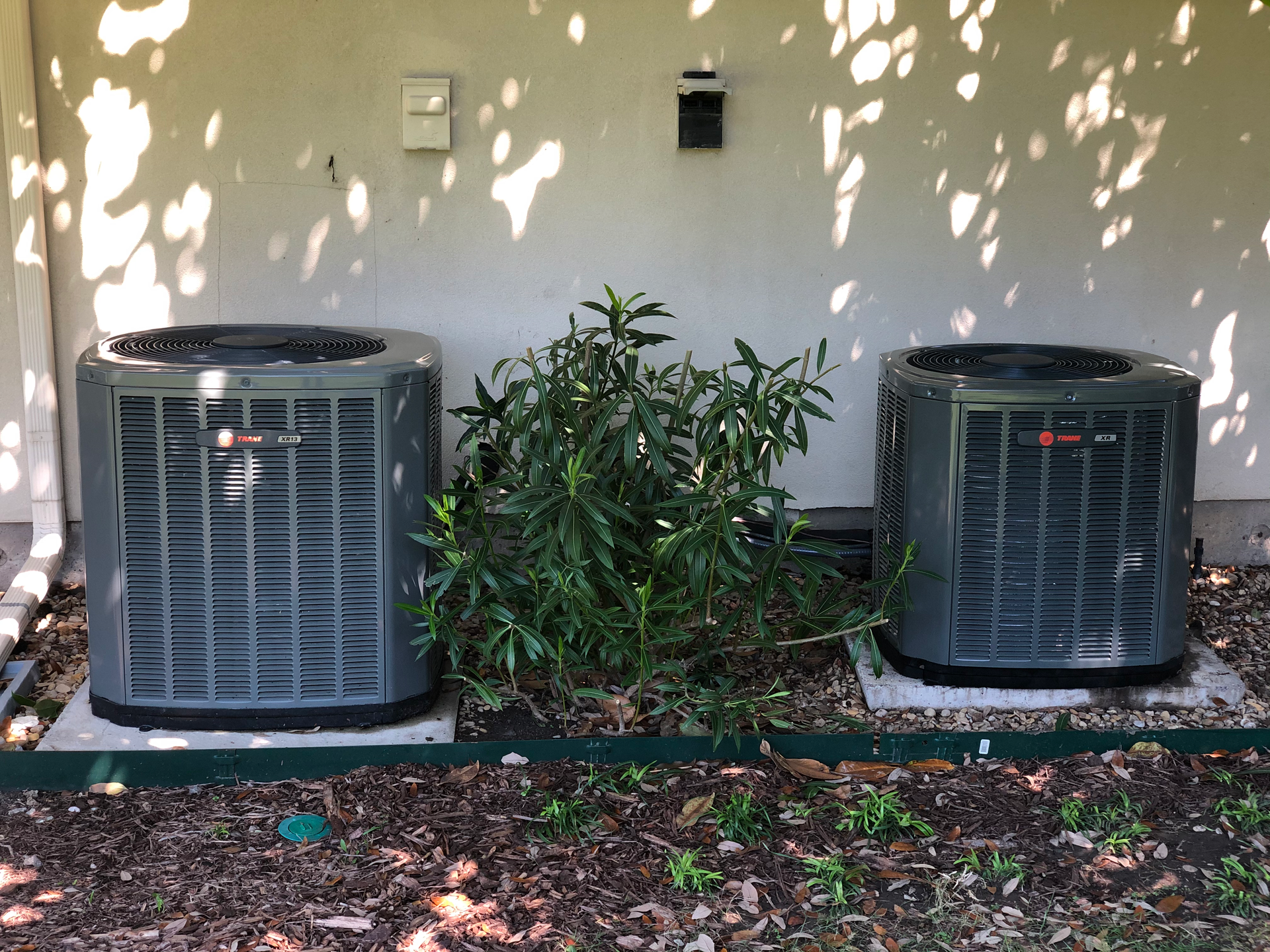 Two air conditioners are sitting next to each other on the side of a building.