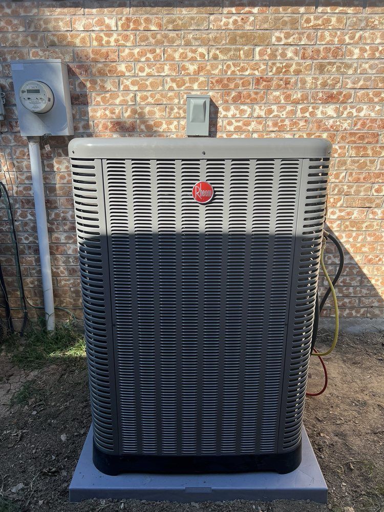 A large air conditioner is sitting in front of a brick wall.