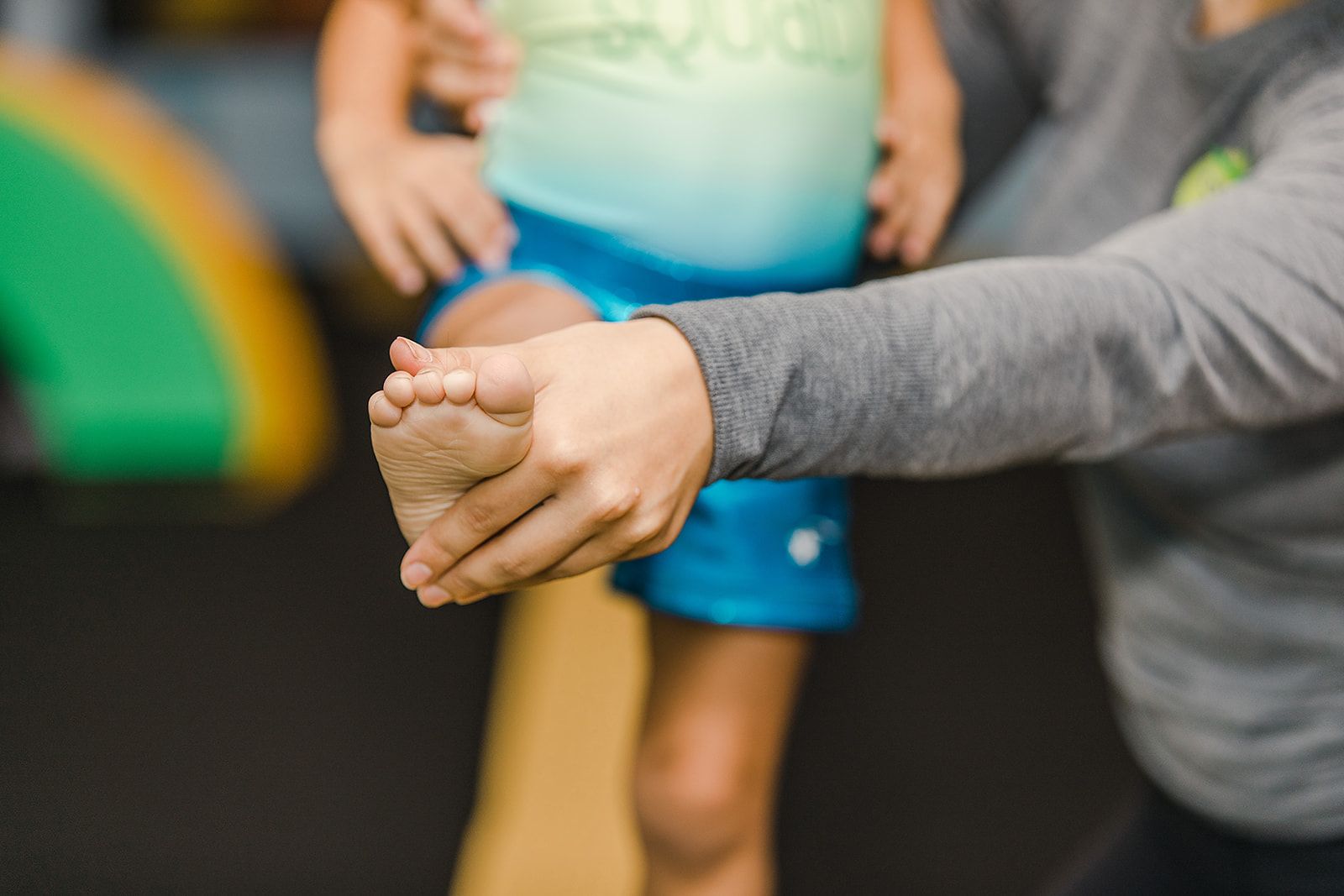 Person helping child with physical therapy, holding foot.