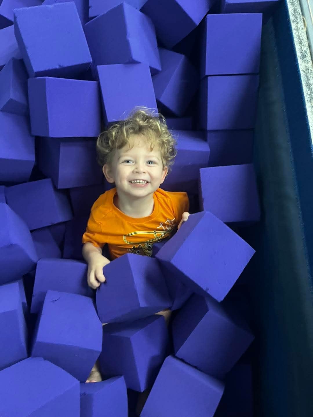 A group of children are playing in a pile of colorful foam cubes.