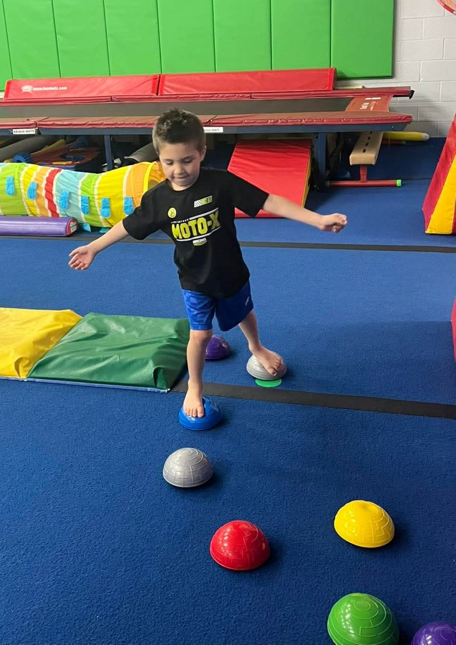A young boy in an orange shirt is climbing a rope