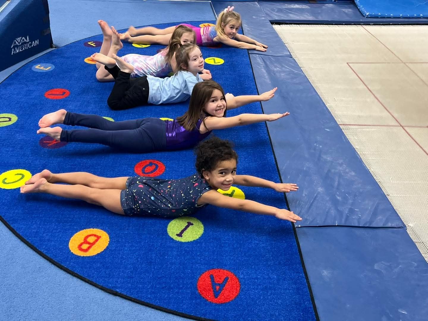 A young girl is sitting on a balance beam in a gym.
