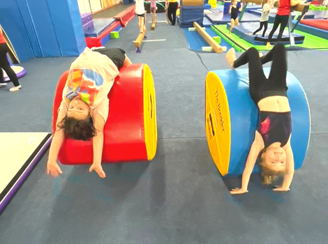 Two children upside down on colorful gymnastics barrel mats in a gym.