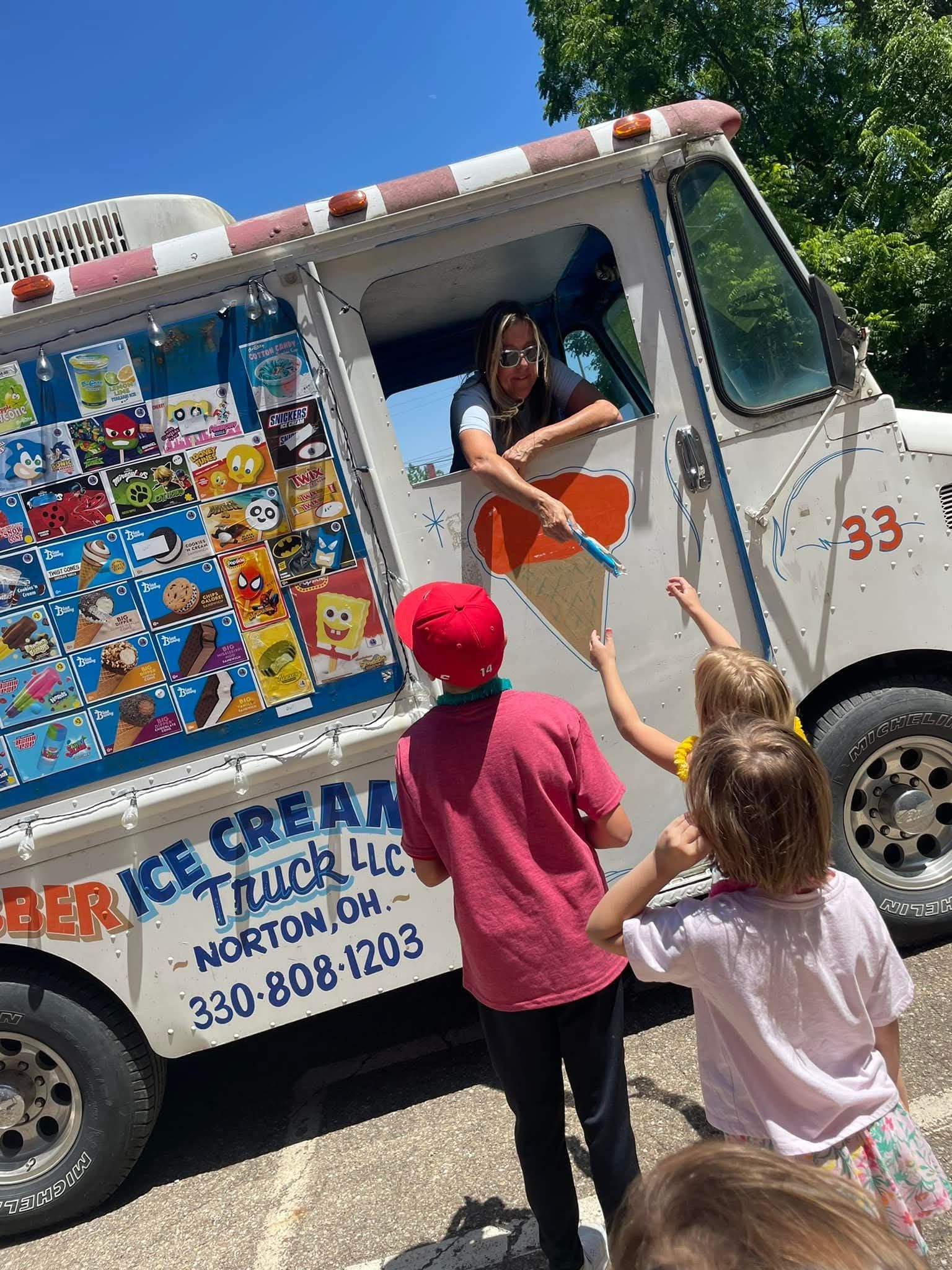 Children reaching toward ice cream truck window to receive treats.