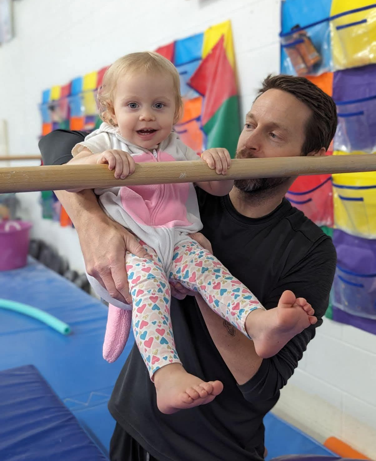 A baby in a striped tank top is hanging from gymnastic rings