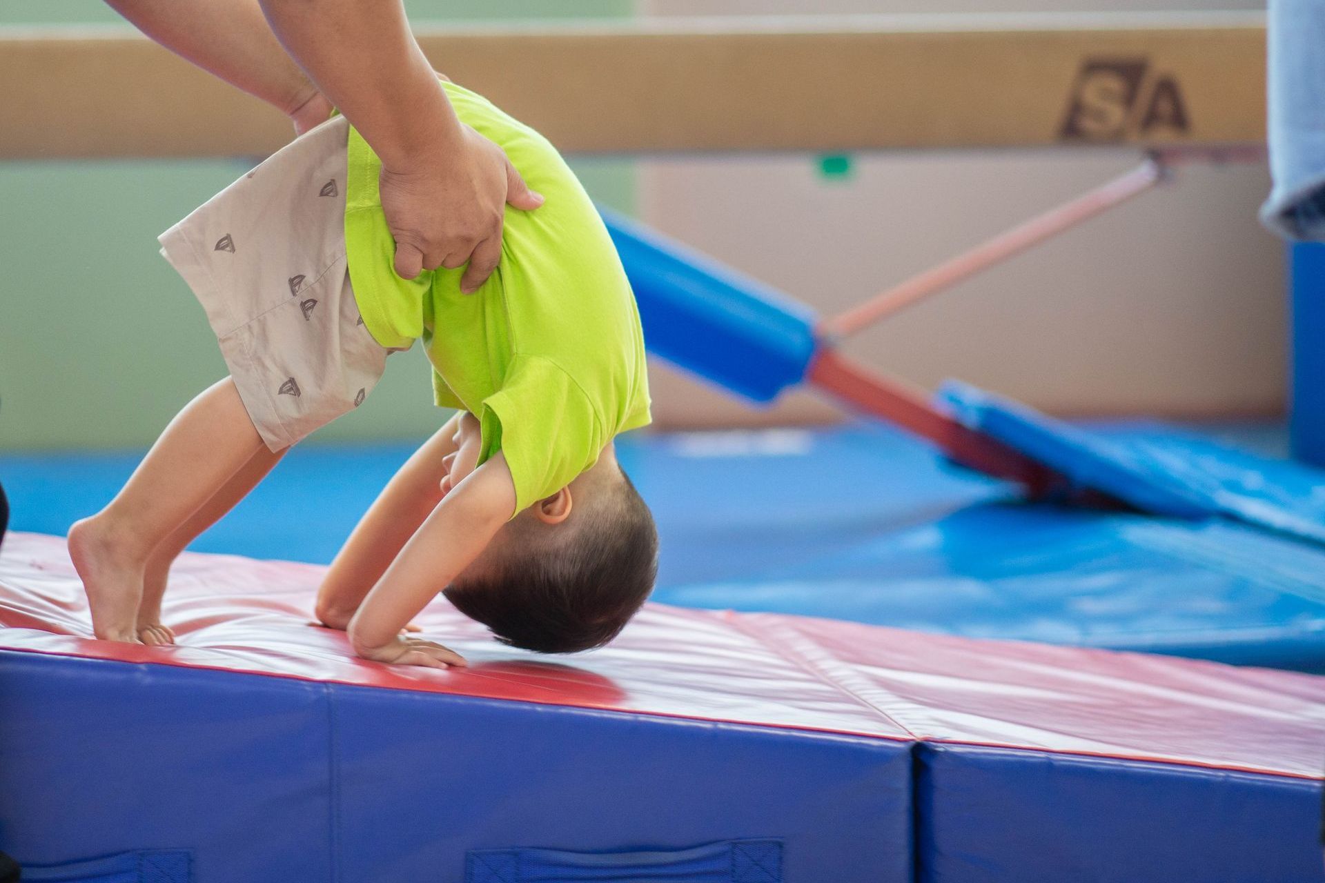 A young boy is doing a handstand on a mat in a gym.