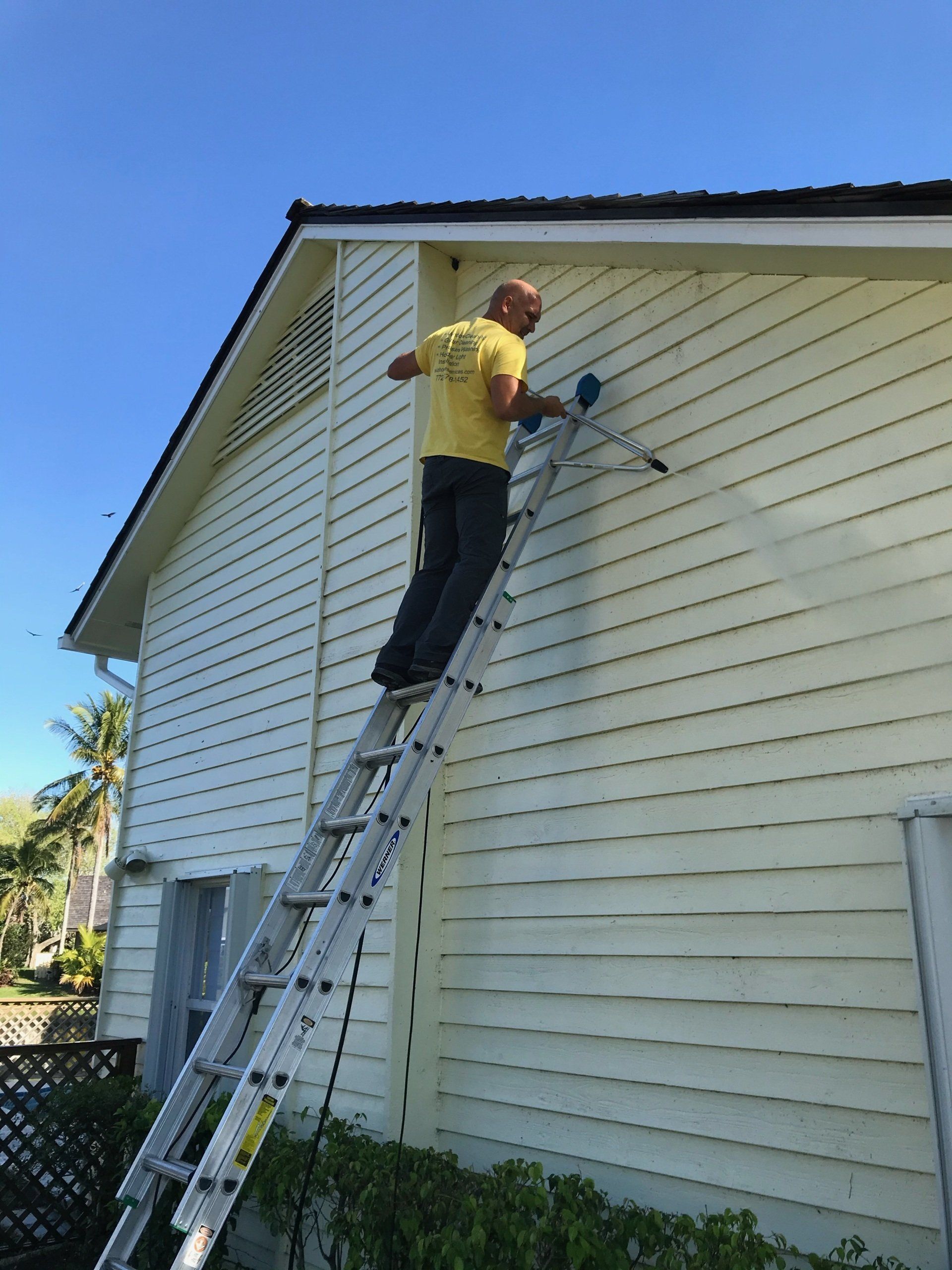 Worker pressure cleaning a house