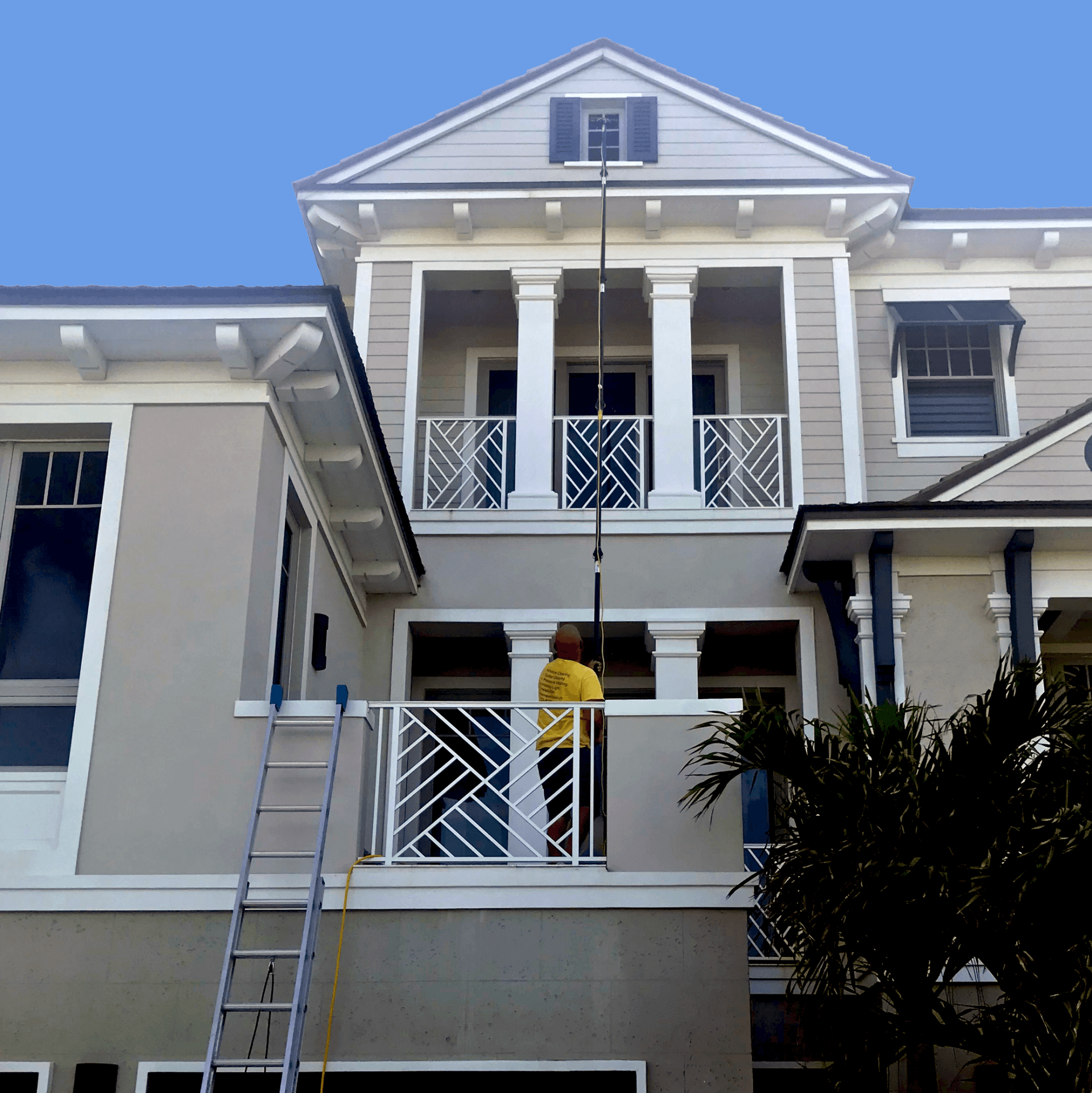 Man cleaning windows with an extender on a tan home with white balconies 