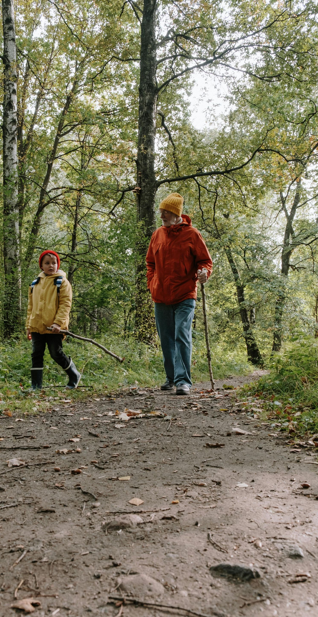 Two people walking on a forest path in autumn, wearing red and tan jackets.