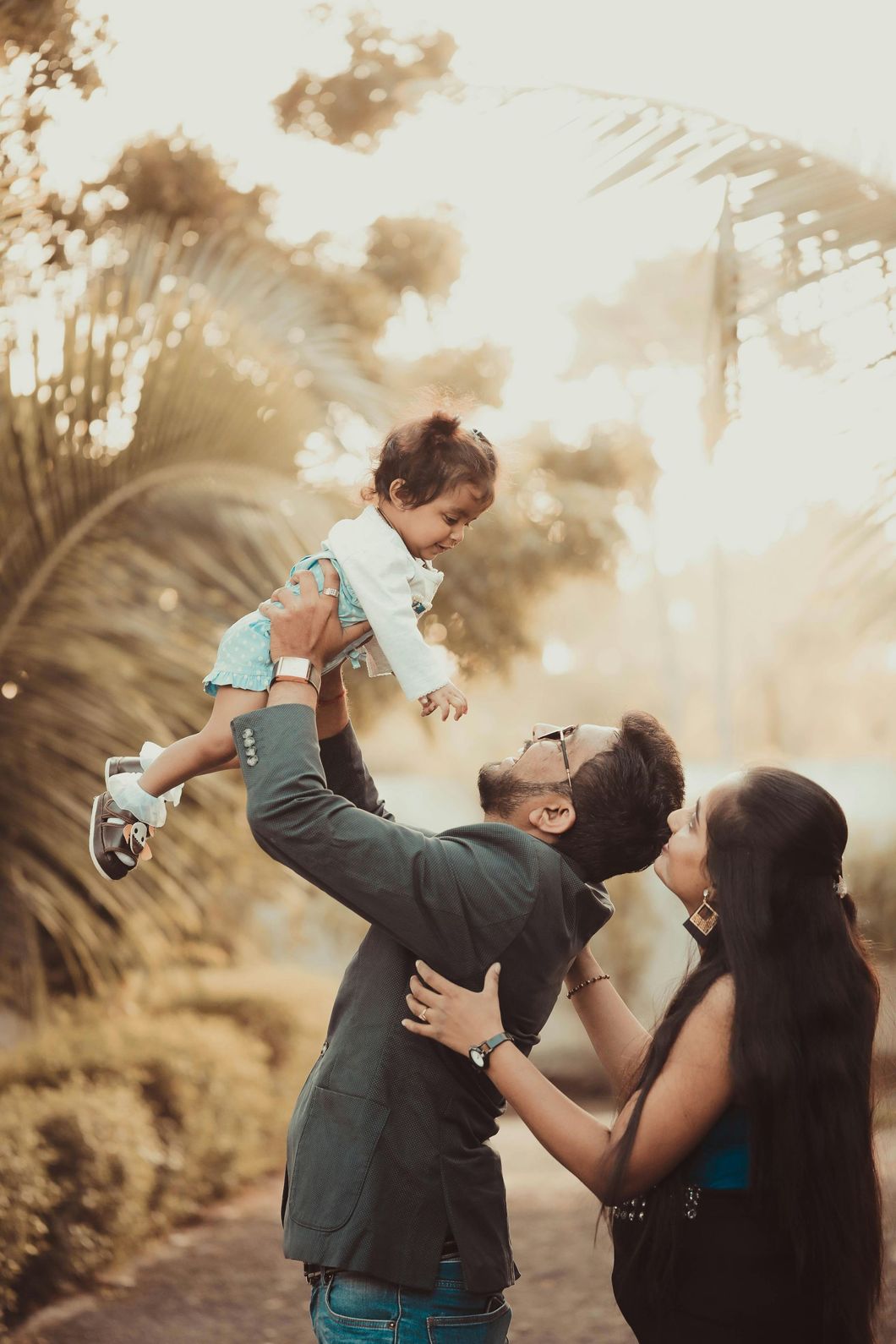Family lifting a child outdoors in warm sunlight, with palm trees in the background