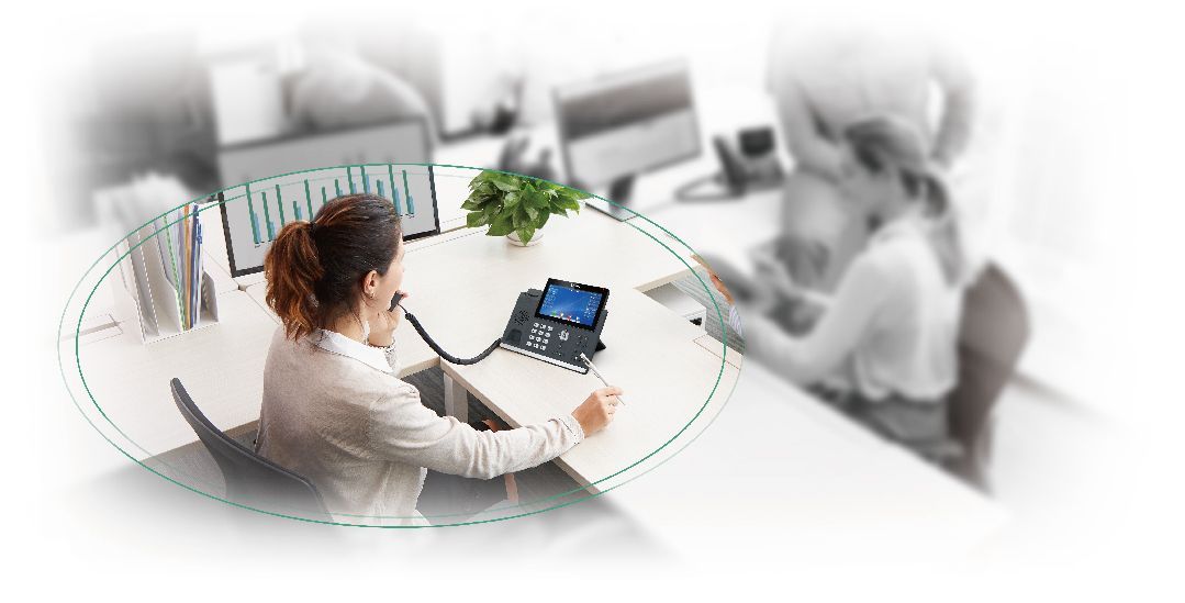 A woman is sitting at a desk talking on a phone.