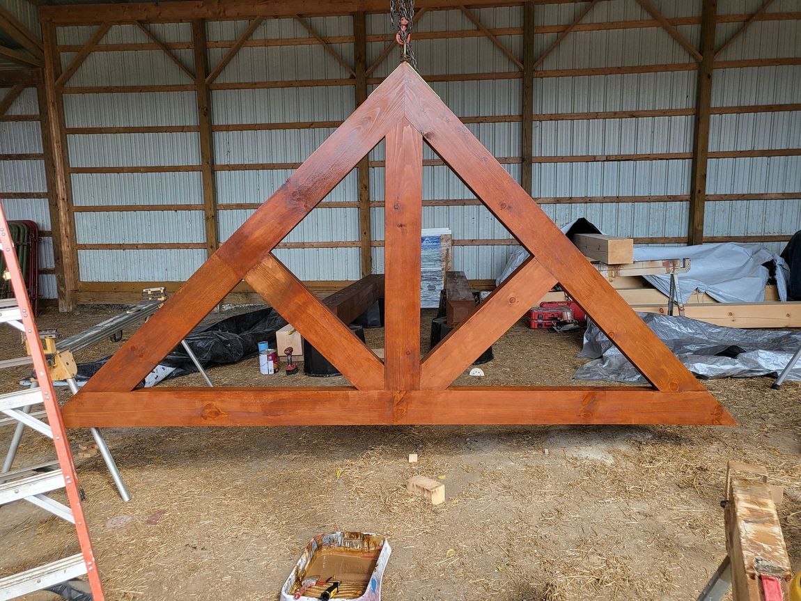 Large wooden truss frame in a barn workshop with tools and materials scattered nearby