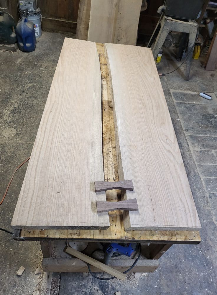 Two light wood slabs on a workbench with a rough live edge seam down the center