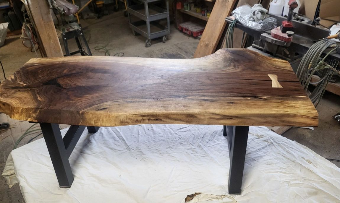 Live-edge wooden table with black metal legs in a workshop, resting on a white tarp.