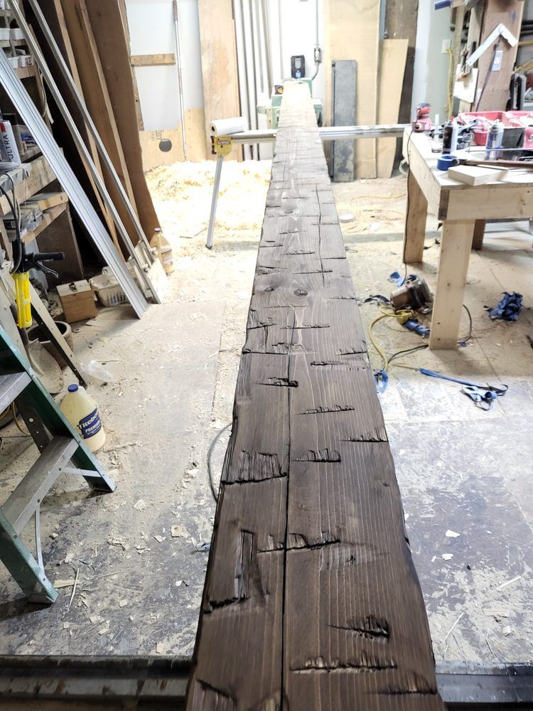 Long weathered wooden beam on a workshop floor amid tools and sawdust