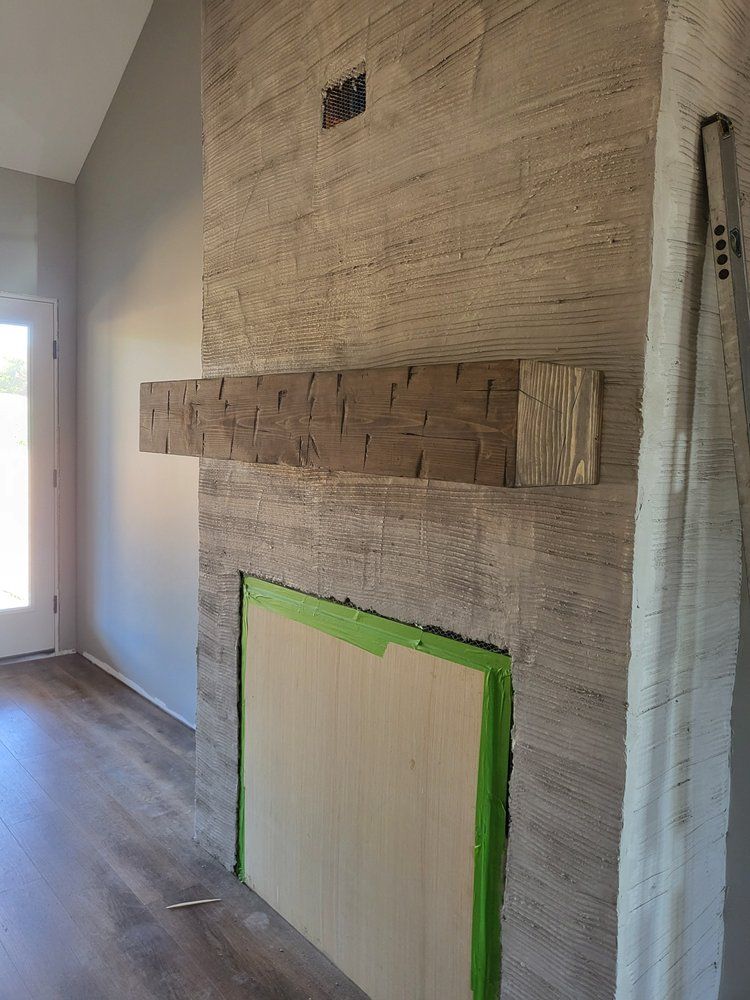 Interior wall with unfinished fireplace surround, green painter’s tape, and wood floor.