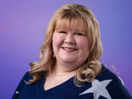 Smiling woman in a navy sweater with a silver star against a purple background