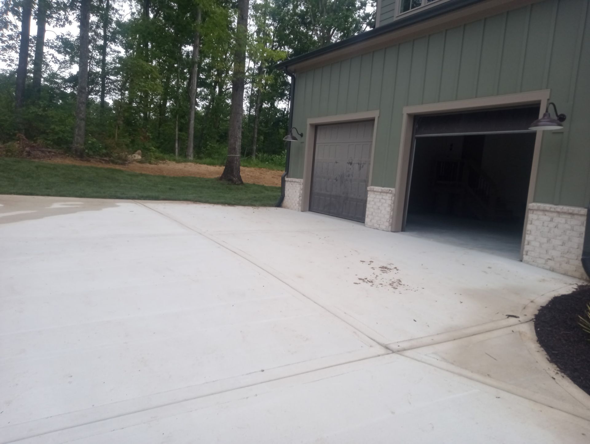 Concrete driveway beside a green garage with two open bays and trees in the background