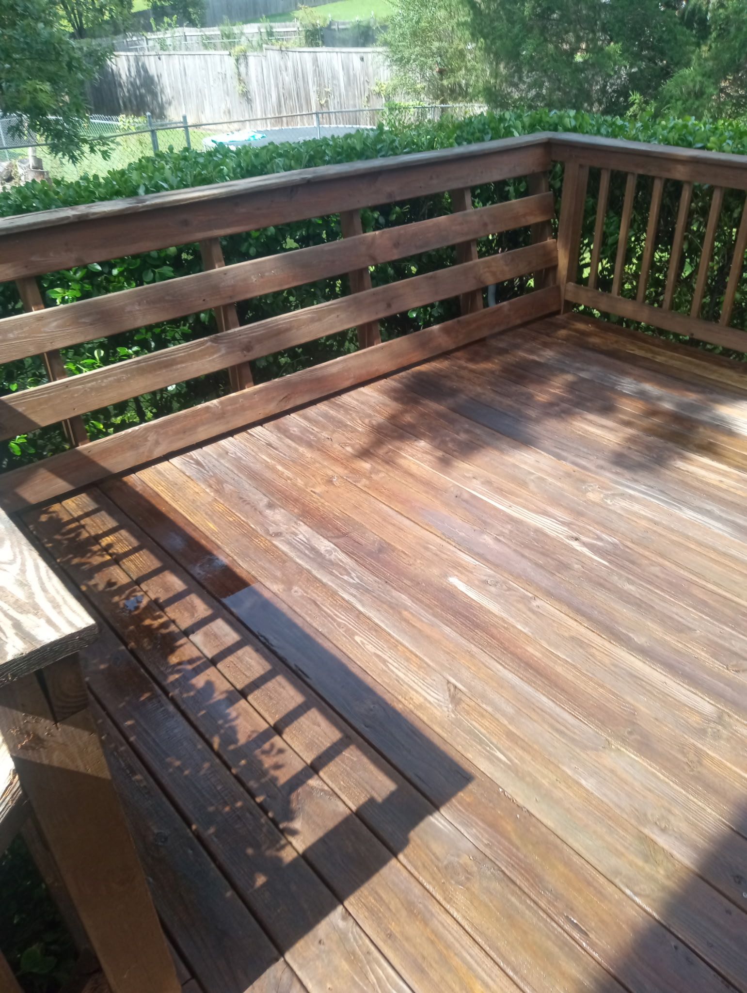 Wooden deck with railing in sunlight, overlooking green trees and a river.