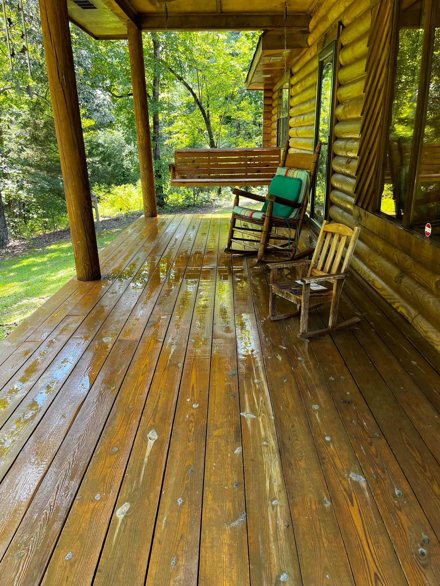 Wooden porch with wet planks, two rocking chairs, and a porch swing. Sunlight streams through the trees.