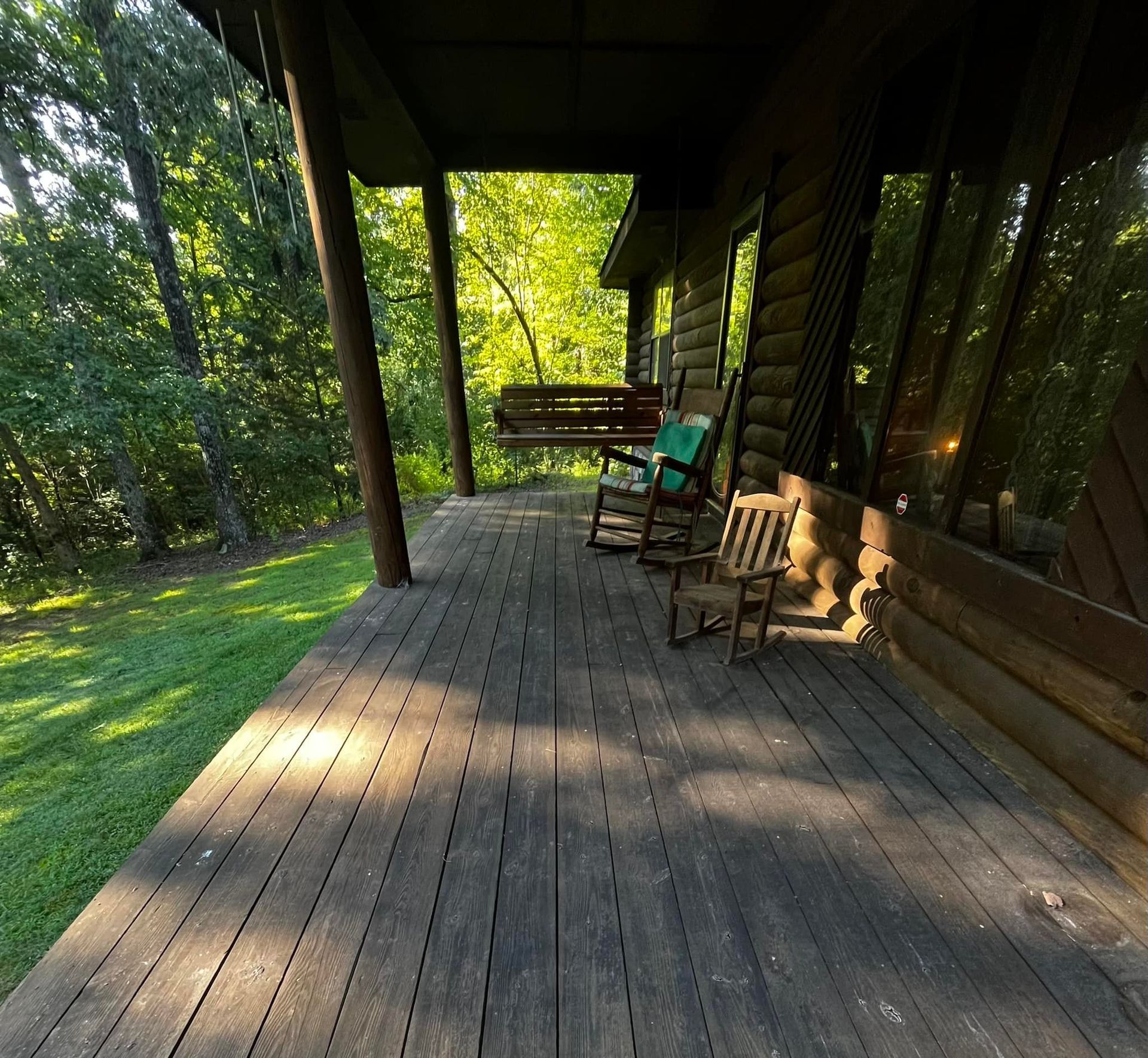 Wooden porch of a cabin with rocking chairs, a swing, and a view of the forest.