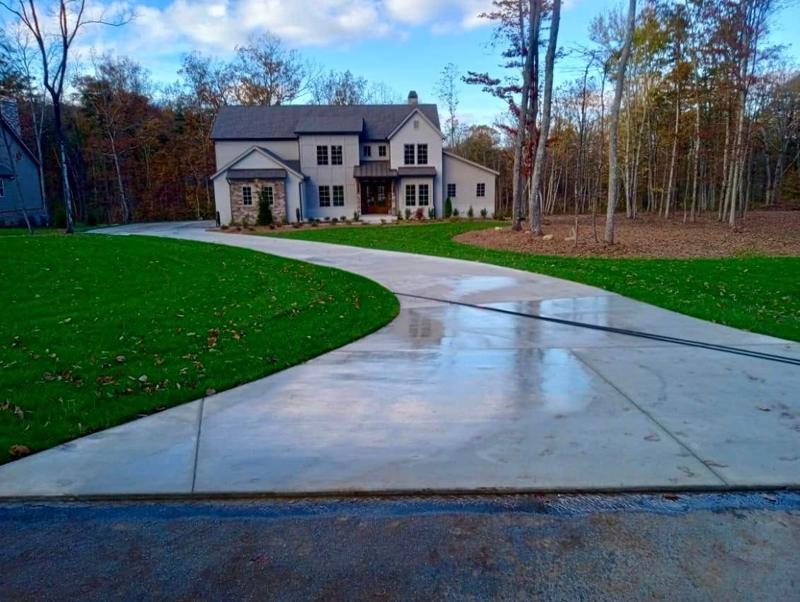 Two-story house with long, curved concrete driveway surrounded by green lawn and trees.