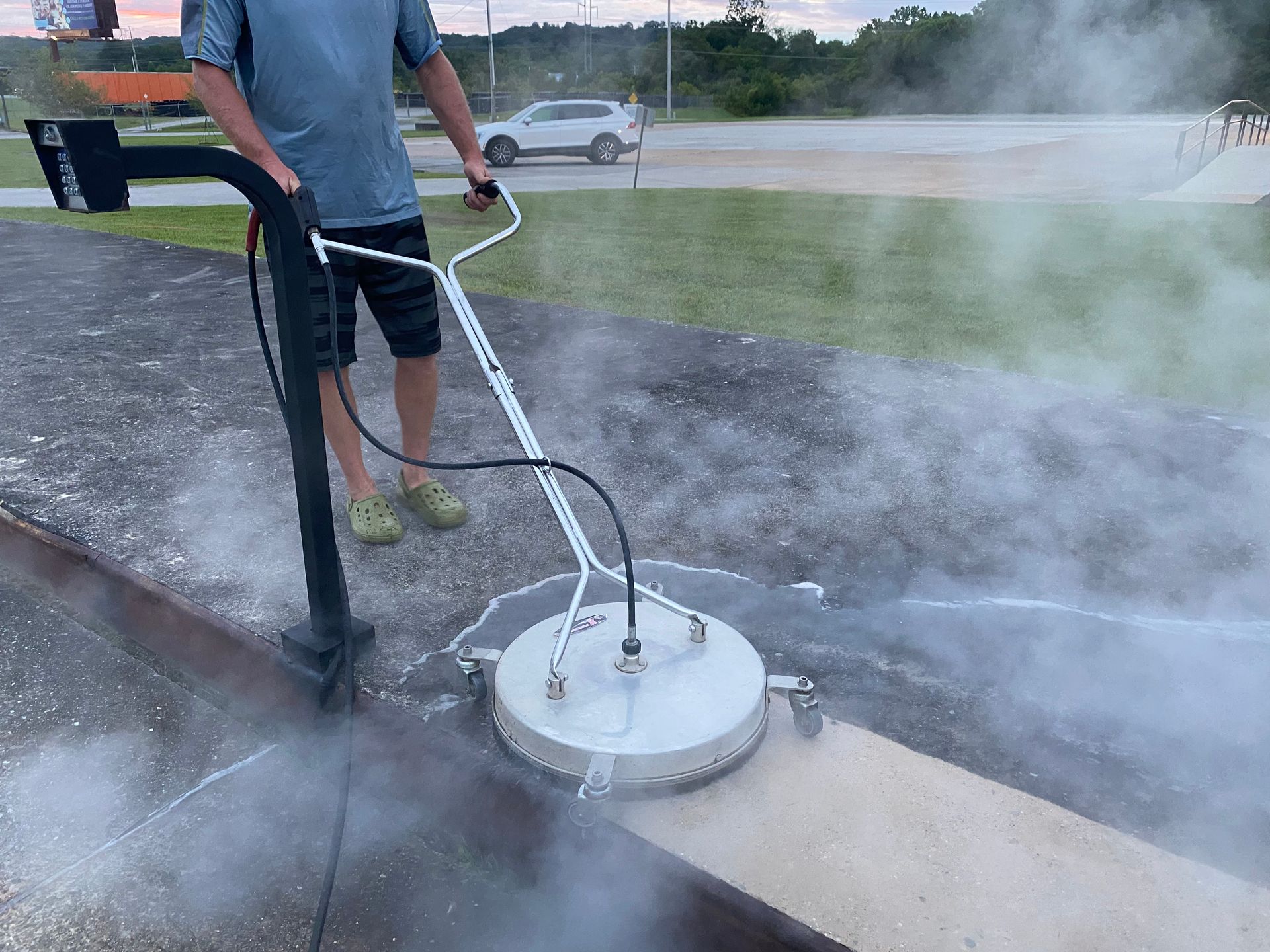 Person using a surface cleaner on a concrete sidewalk, creating steam.