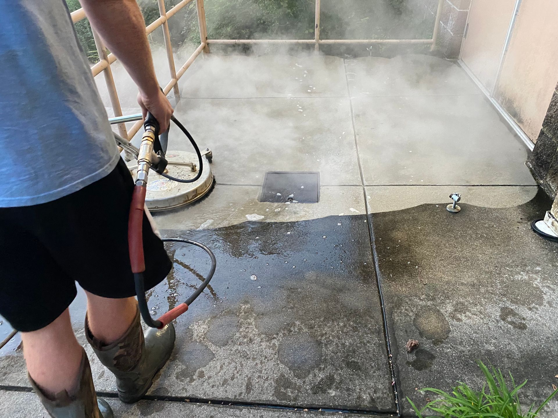Person power washing a concrete patio, creating steam.
