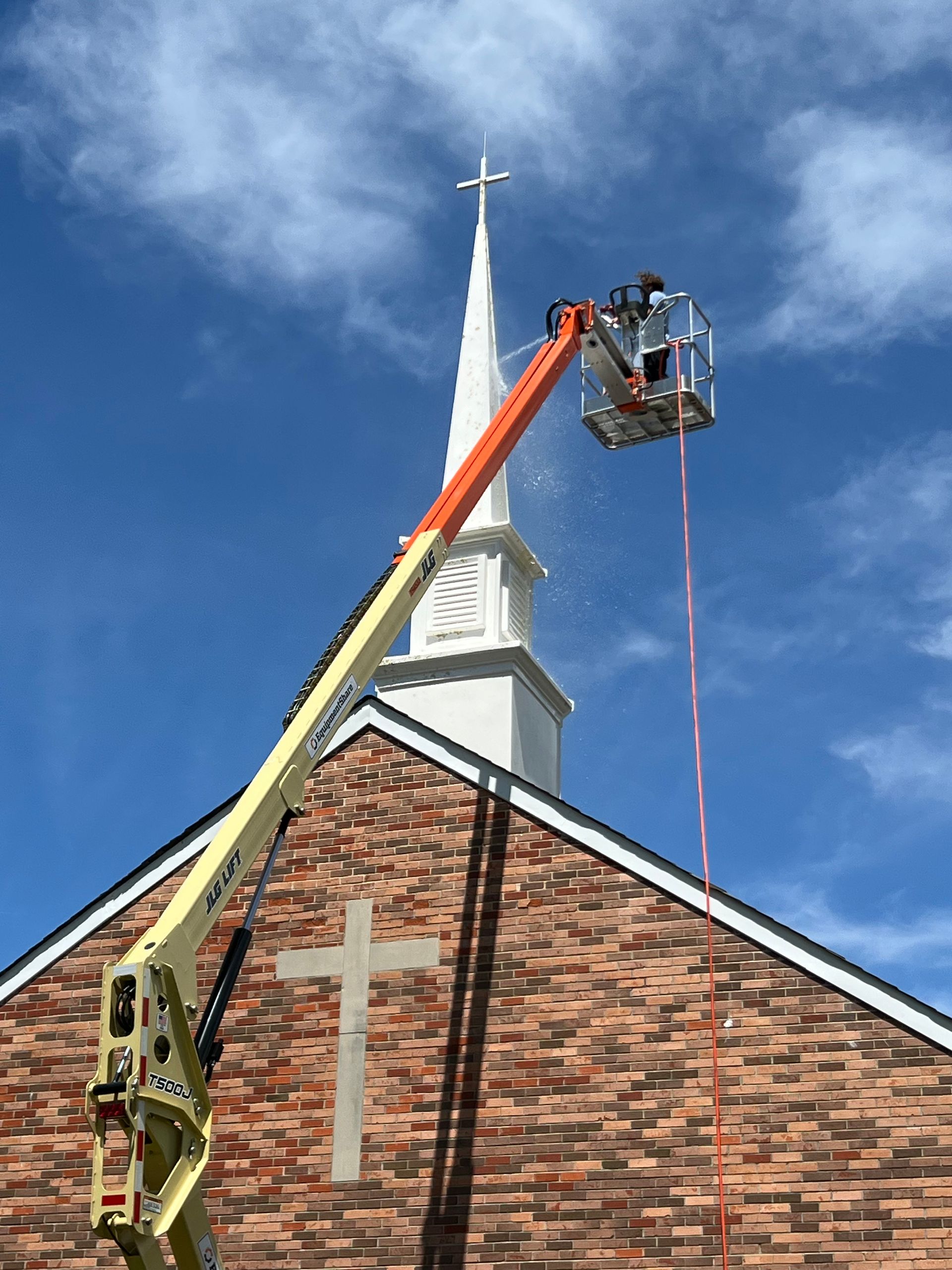 Man on ropes power washing brick building.