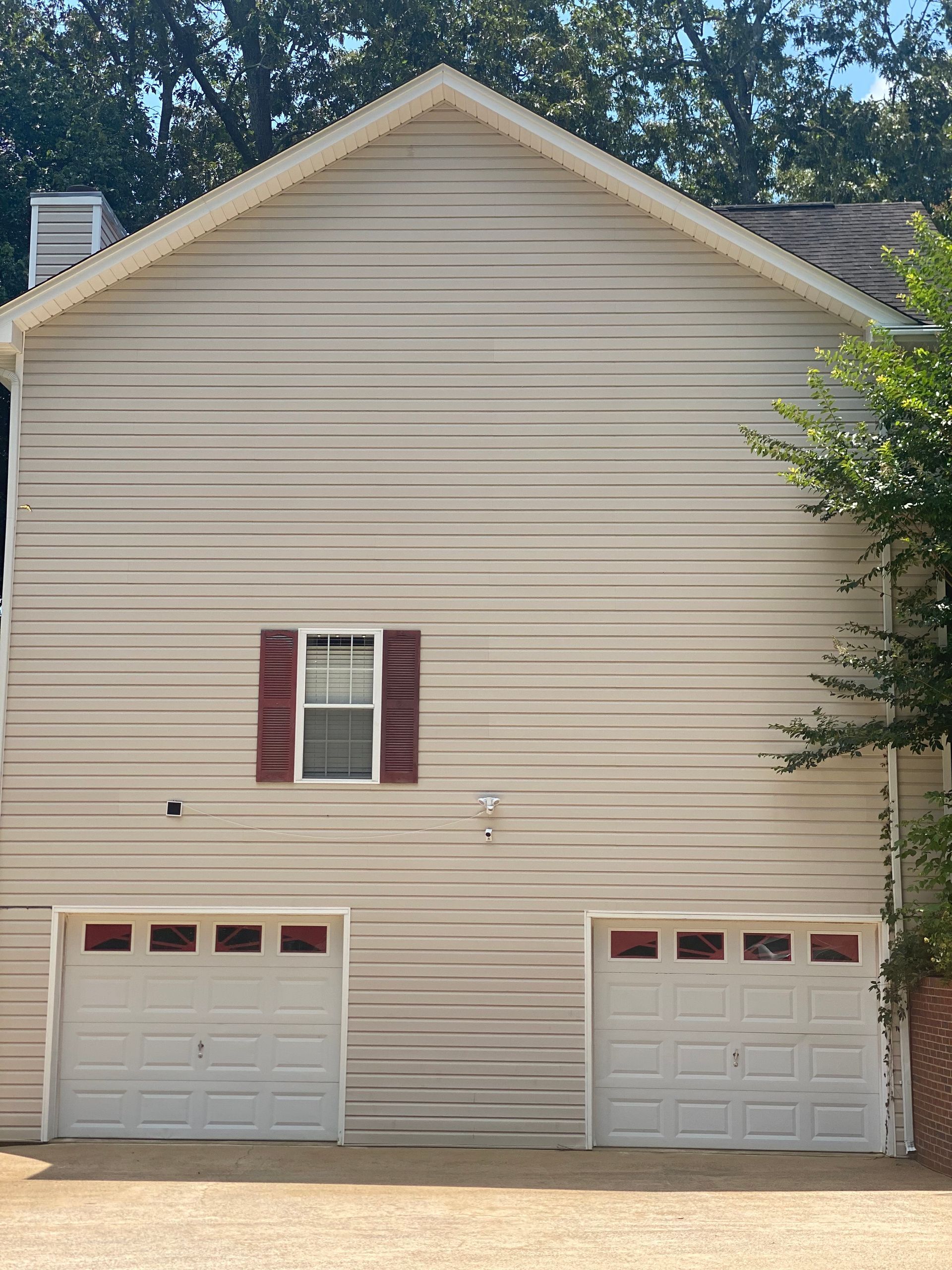 Two-car garage with tan siding, red-framed window, and white garage doors.