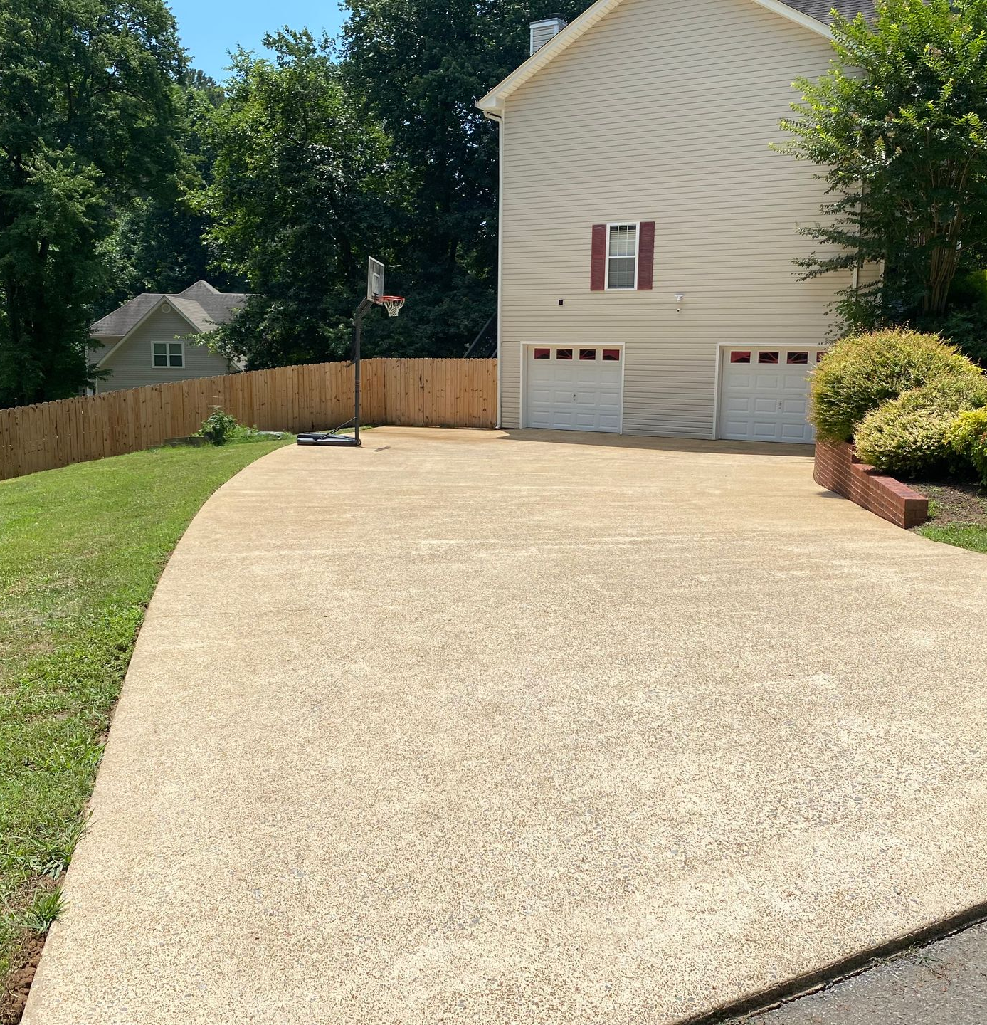 Wide concrete driveway leading to a two-car garage beside a house and fenced backyard on a sunny day
