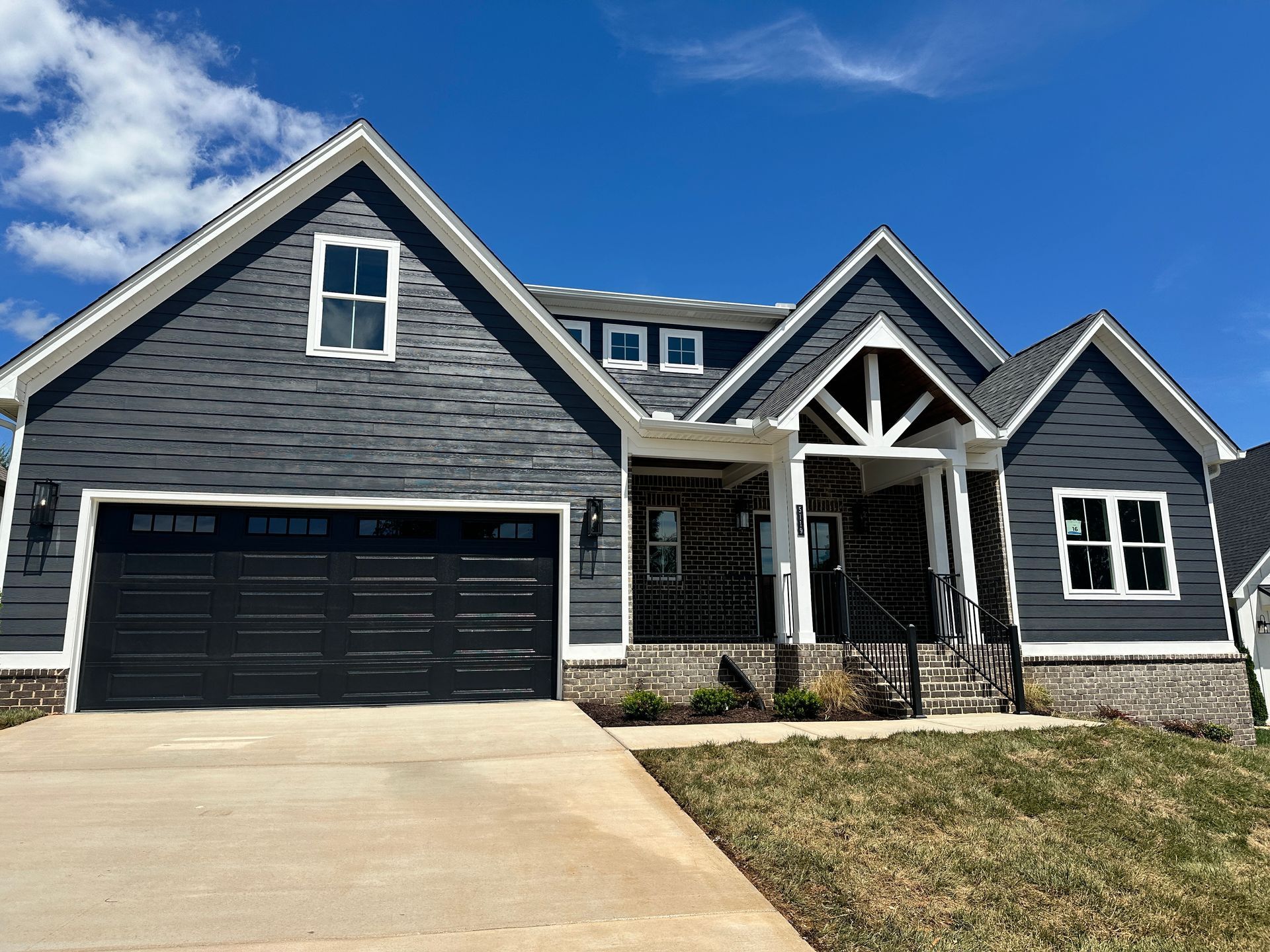Gray suburban house with black garage door, white trim, and stone entry under a blue sky
