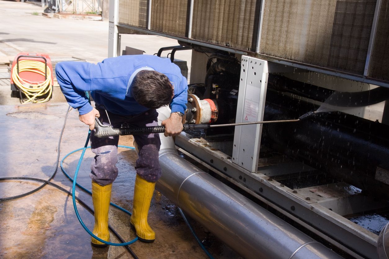 Man in blue cleaning metal pipes with pressure washer, outside.