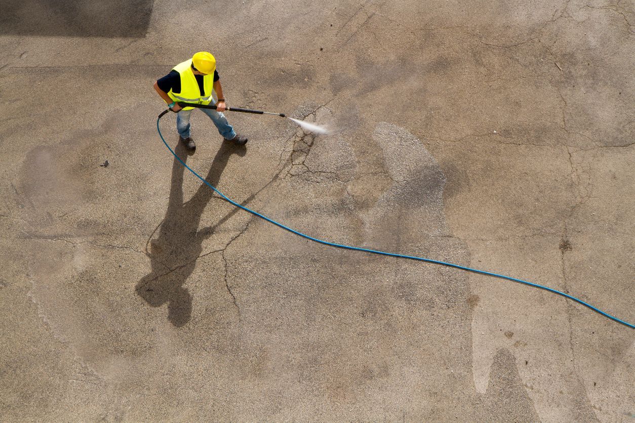 Worker in safety vest pressure washing a concrete surface.